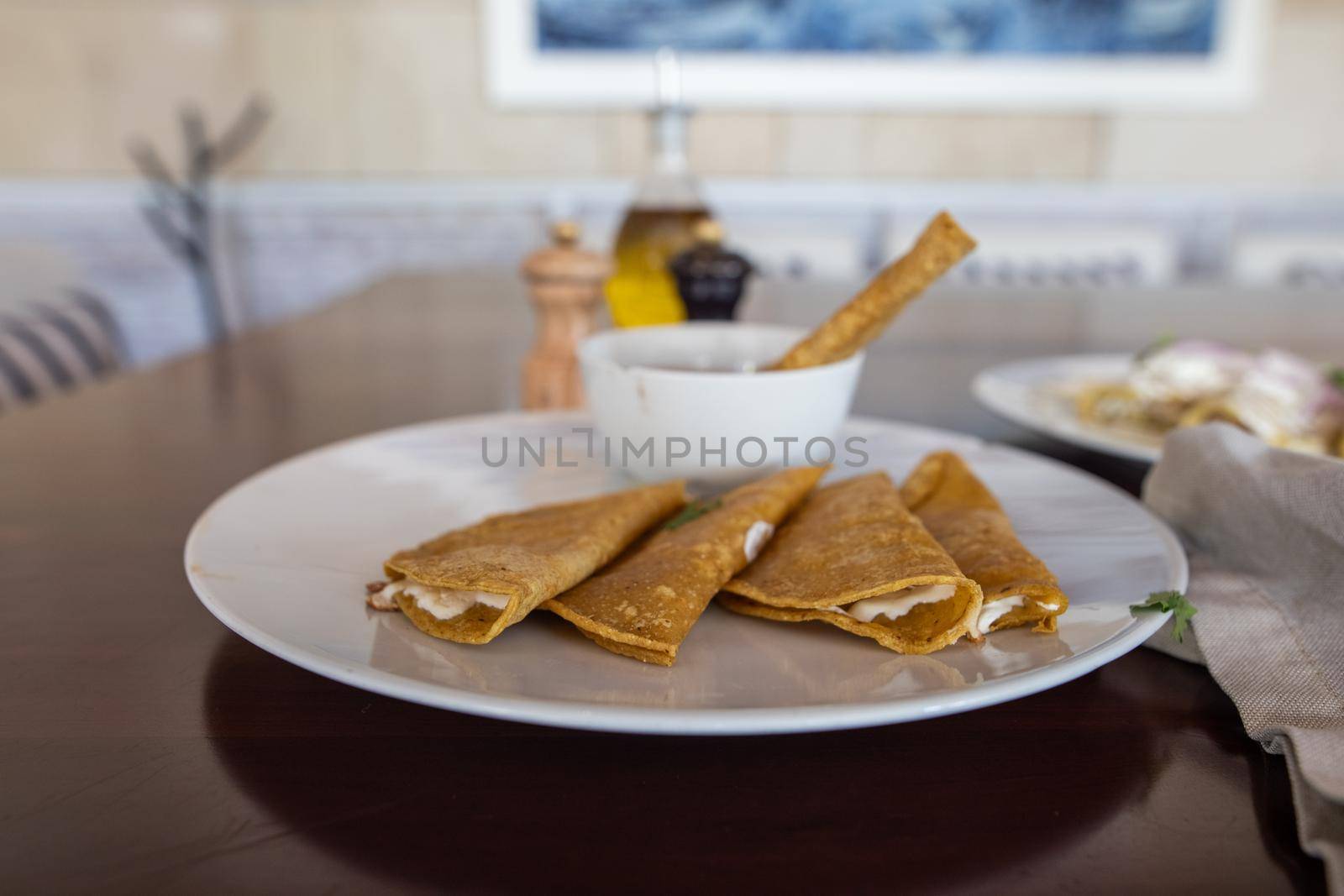 Close-up of plate with five delicious quesadillas and cup of beans on brown table with blurry background. Spices and authentic Hispanic snacks on wooden surface. Traditional Mexican cuisine
