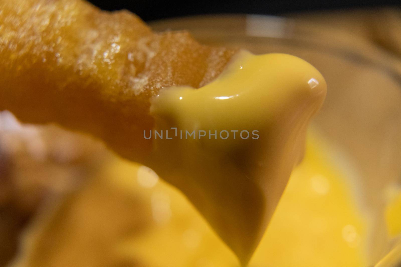 Close-up of melted cheddar cheese on wavy French fry above blurry background. Fried potato snack covered with tasty yellow dip. Delicious fast food preparation