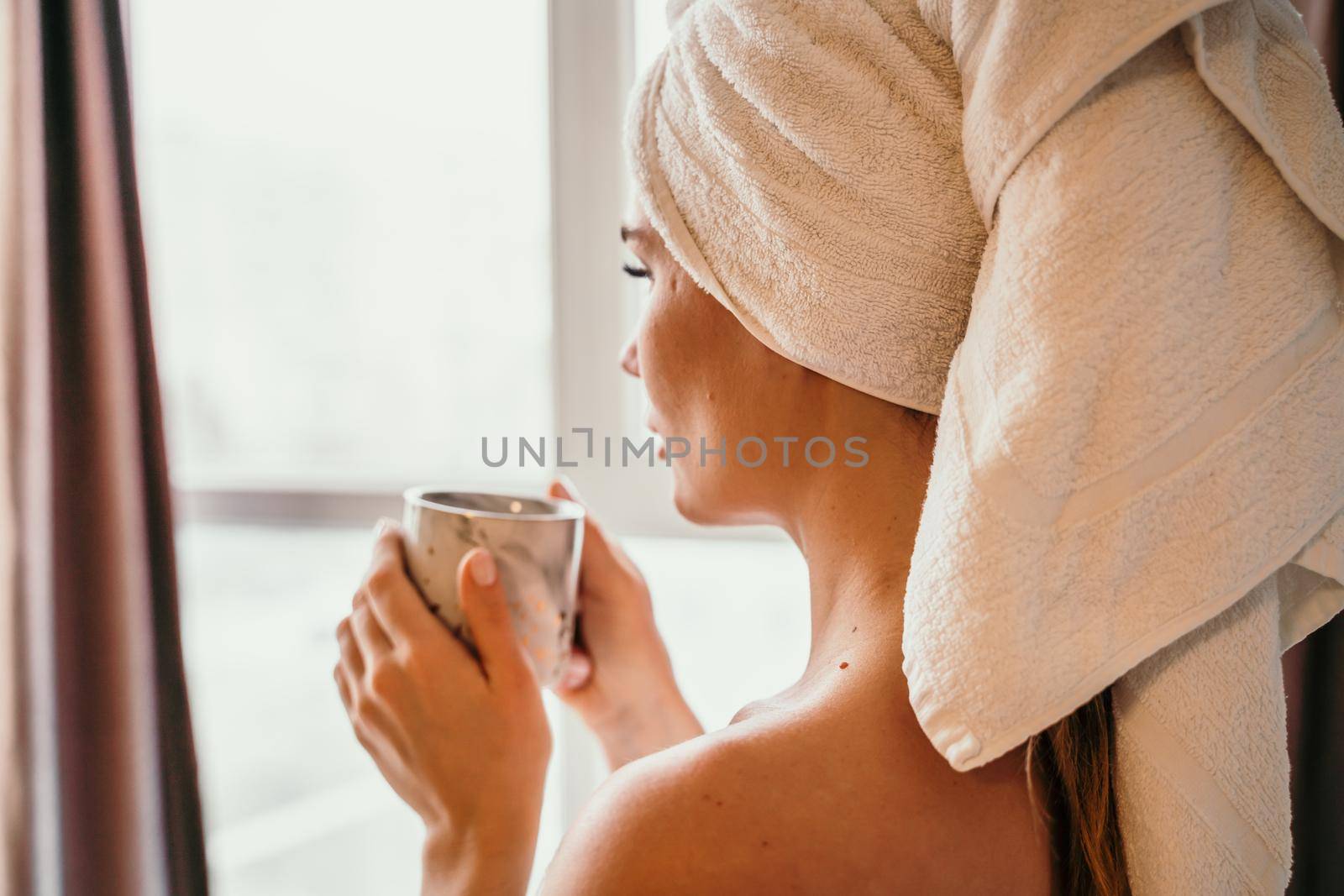 Young serene relaxed woman in spa bath towel drinking hot beverage tea coffee after taking shower bath at home. Beauty treatment, hydration concept. by Matiunina