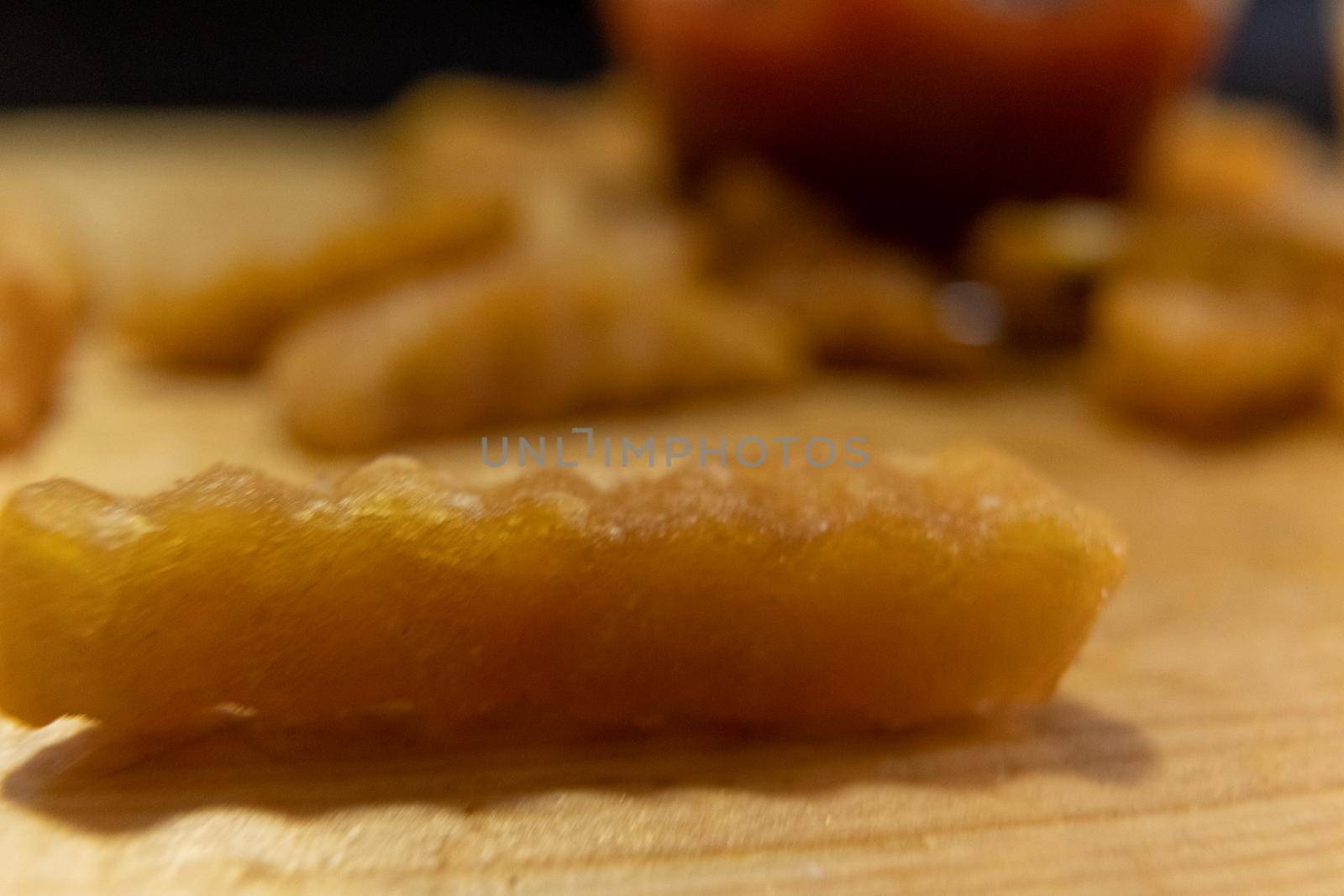 Extreme close-up of wavy French fry on wooden surface with blurry cup of ketchup as background. Tasty fried snacks and glass of red tomato dressing. Delicious fast food