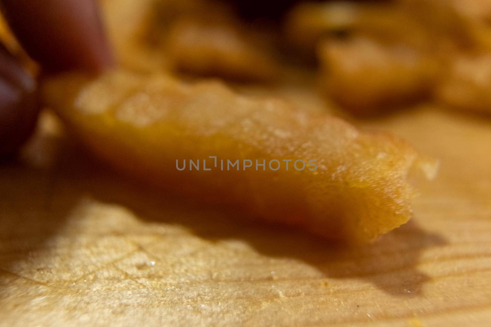 Close-up of fingers grabbing wavy French fry on wooden surface by Kanelbulle