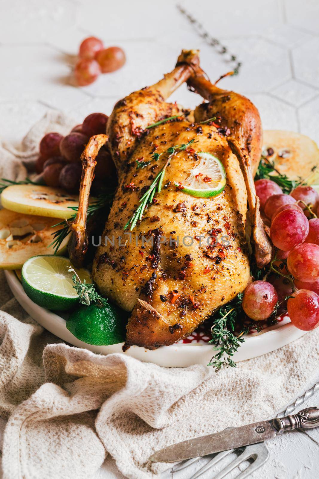A duck baked for Thanksgiving as a symbol of family unification at a common holiday table. Still life in orange tones, shot in a light key on a white ceramic background. The atmosphere of the festival and celebration. The dish is decorated with grapes, lime, quince and aromatic herbs.