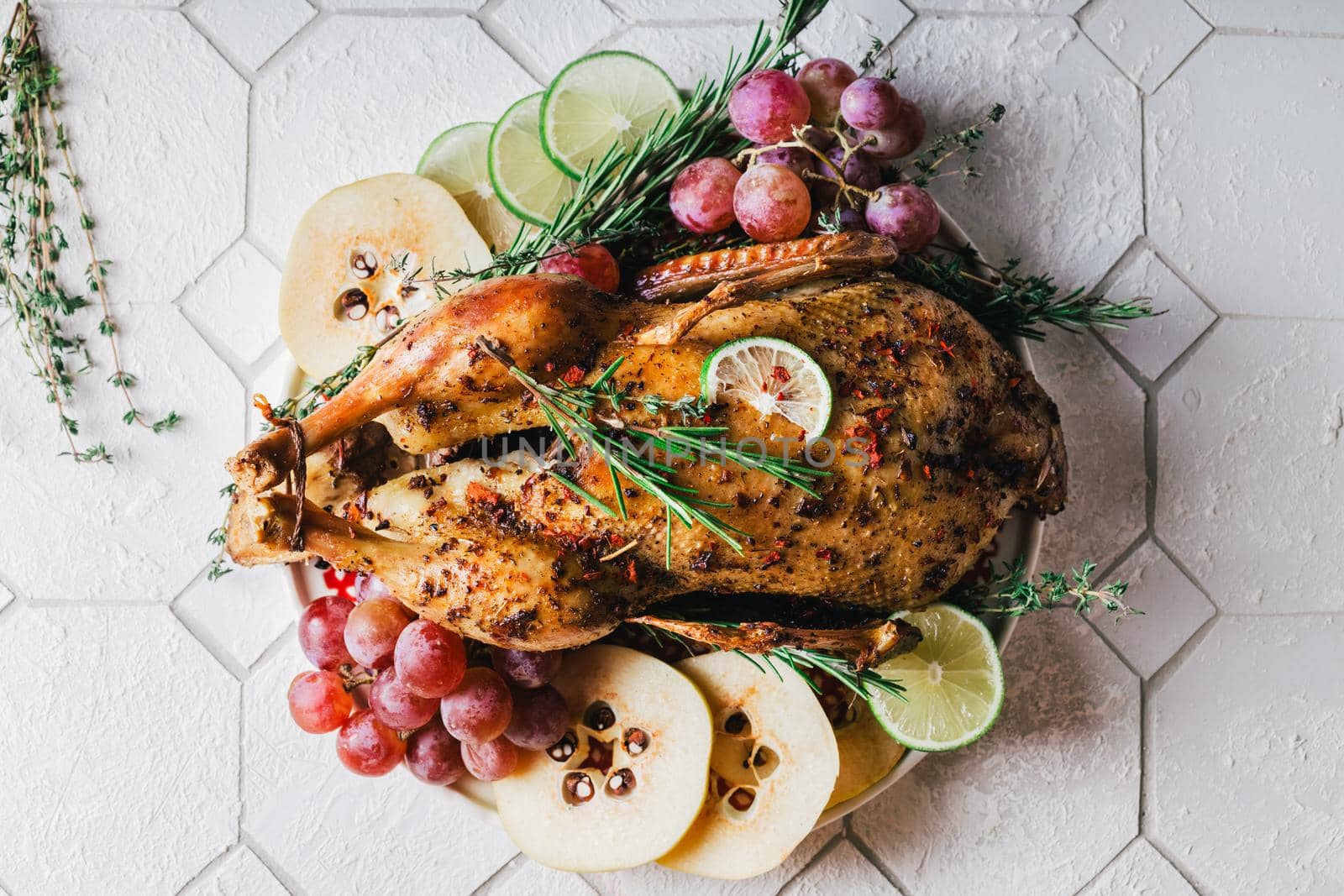 A duck baked for Thanksgiving as a symbol of family unification at a common holiday table. Still life in orange tones, shot in a light key on a white ceramic background. The atmosphere of the festival and celebration. The dish is decorated with grapes, lime, quince and aromatic herbs.