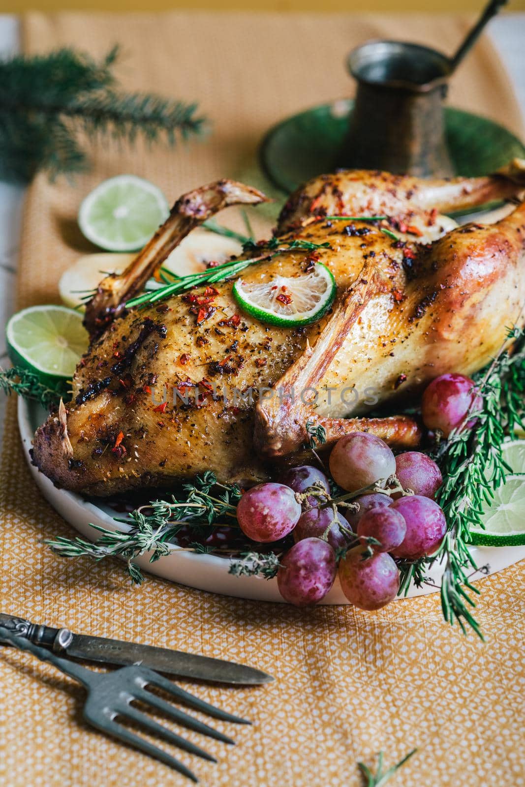 A duck baked for Thanksgiving as a symbol of family unification at a common holiday table. Still life in orange tones, shot in a light key on a white ceramic background. The atmosphere of the festival and celebration. The dish is decorated with grapes, lime, quince and aromatic herbs.