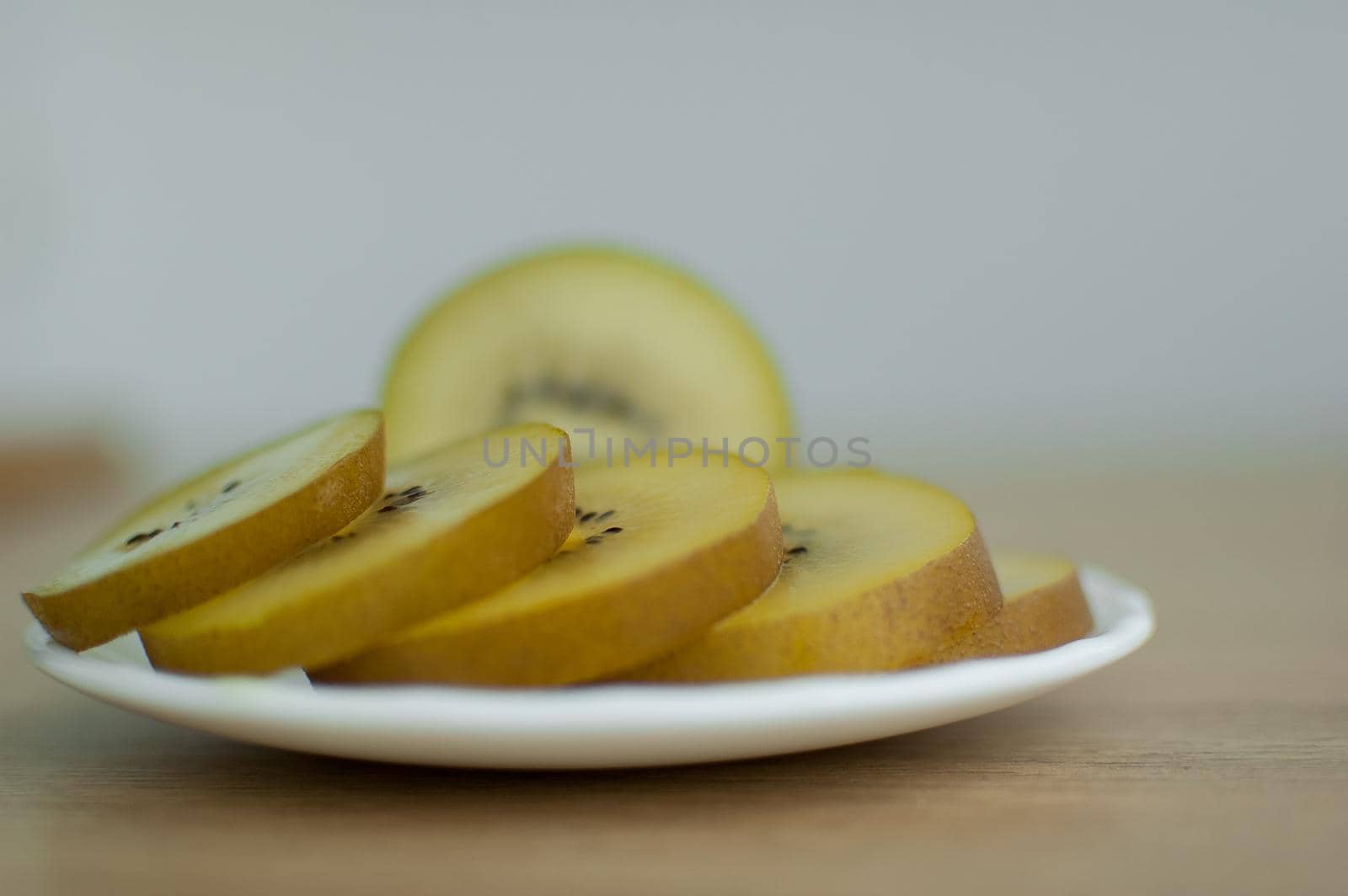 Slices of golden kiwi with yellow pulp on white plate on the kitchen. Exotic fruits, healthy eating concept.