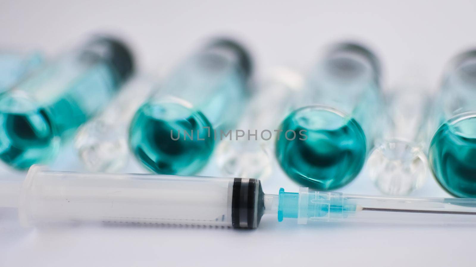 Vial vaccine, top view of glass ampoules with transparent and blue liquid, a syringe is lying near on white background, global vaccination concept by balinska_lv