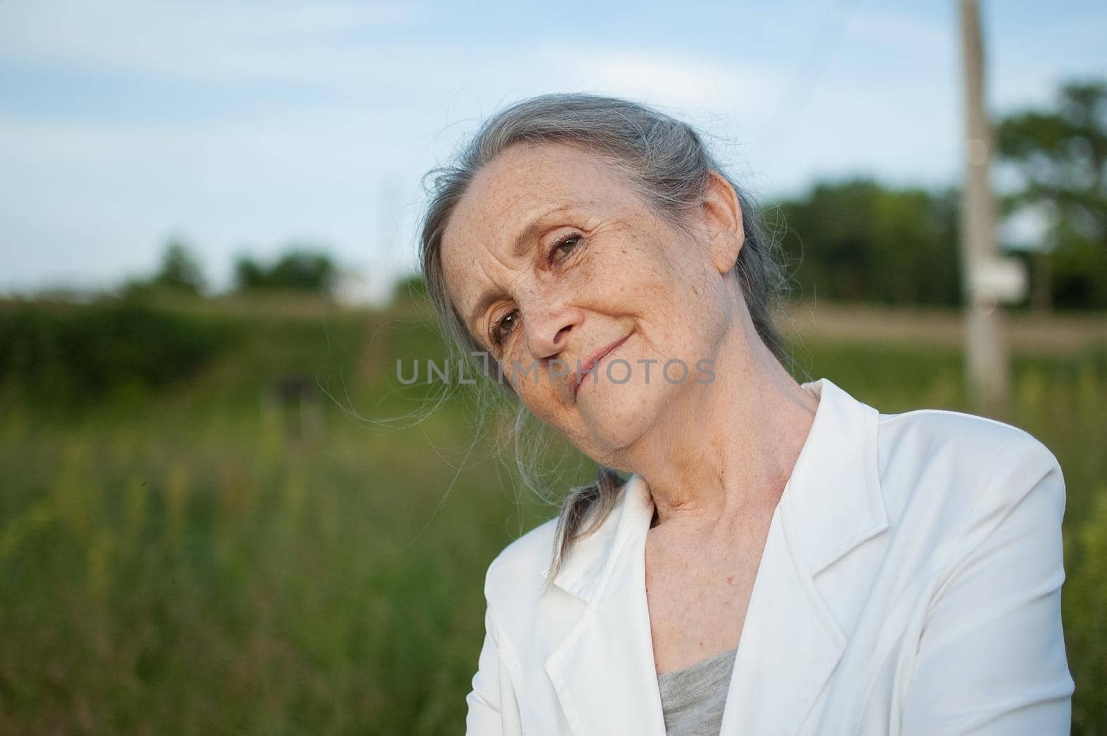 Portrait of senior woman with grey hair and face with wrinkles wearing white jacket and relaxing at park during sunny day, happy retirement, mothers day concepts