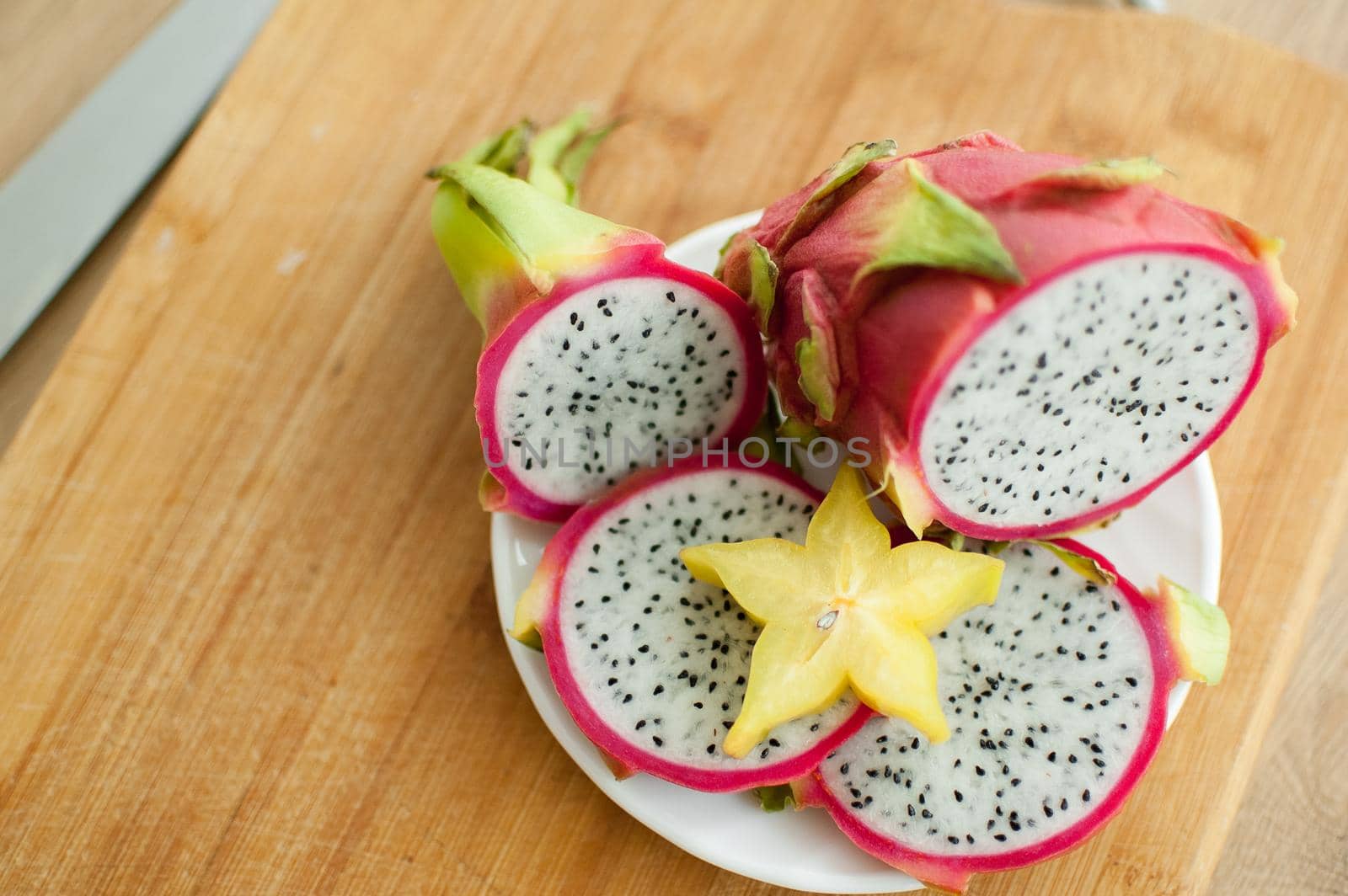 Slices of dragon fruit or pitaya with white pulp and black seeds on white plate with one slice of starfruit or averrhoa carambola. Exotic fruits, healthy eating concept.