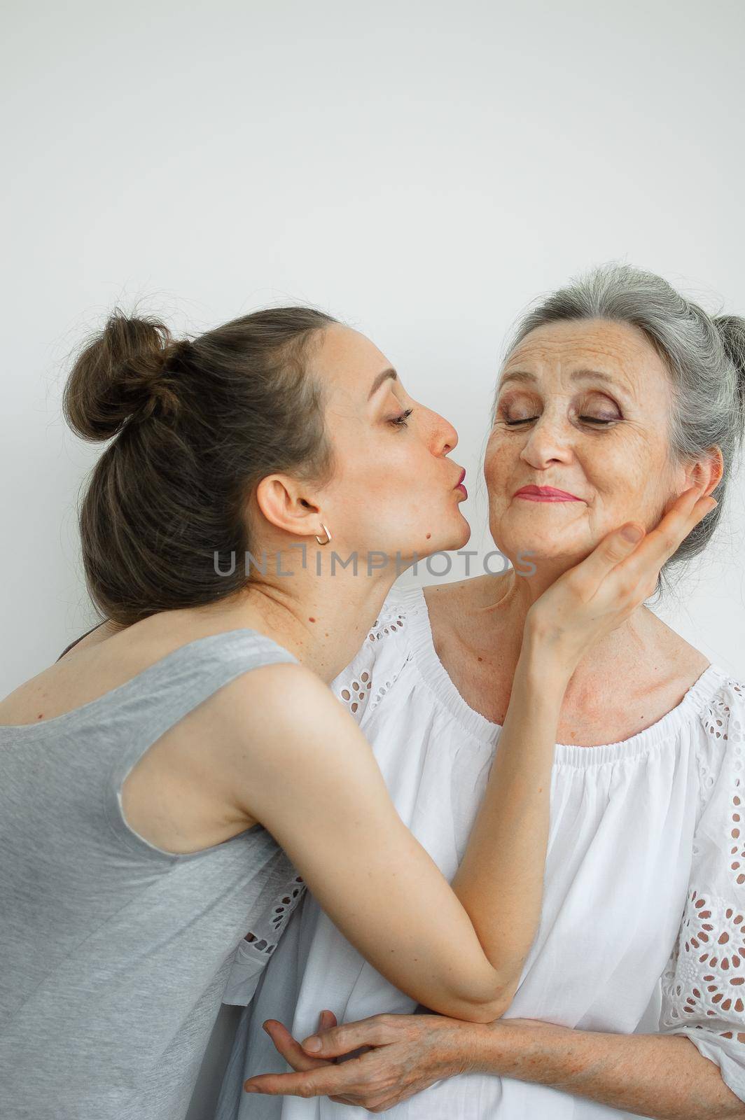 Happy senior mother is hugging her adult daughter, the women are laughing together, sincere family of different age generations having fun on white background, mothers day. by balinska_lv