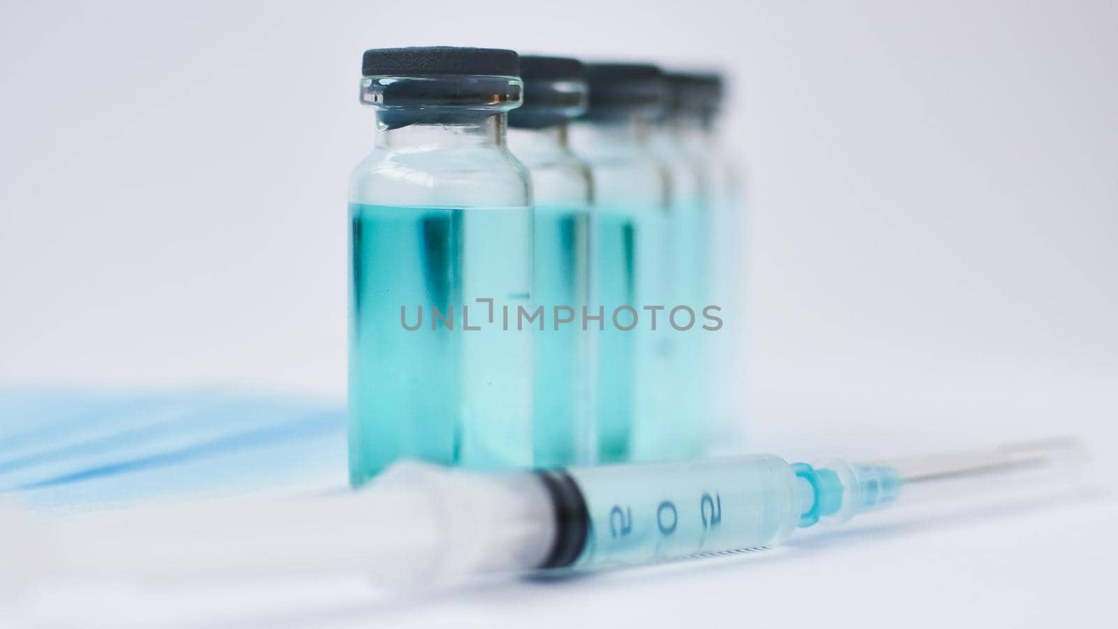Vial vaccine, glass ampoules and a syringe with medical protective mask on white background, global vaccination concept.