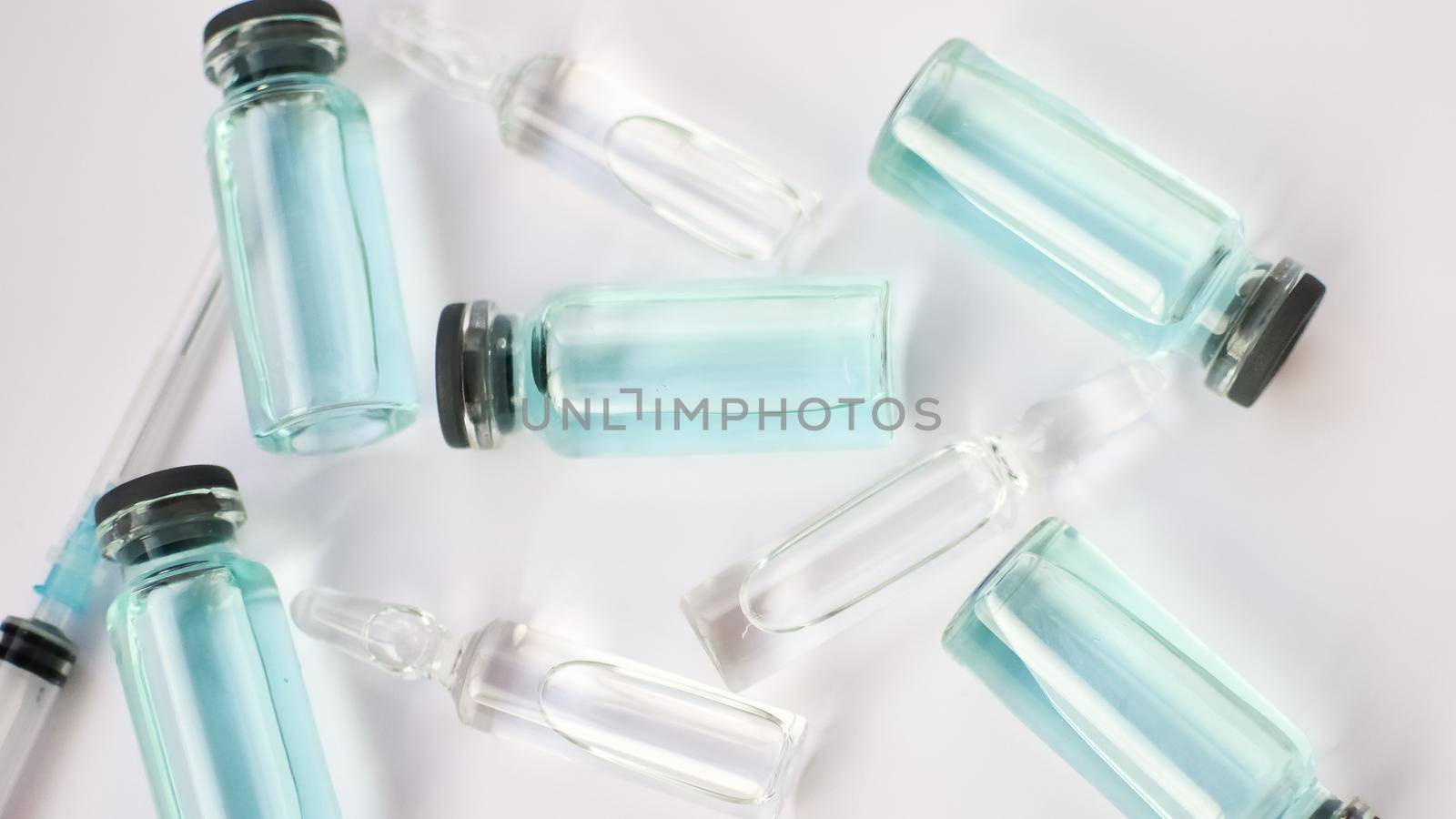 Vial vaccine, top view of glass ampoules with transparent and blue liquid lying on white background, global vaccination concept by balinska_lv