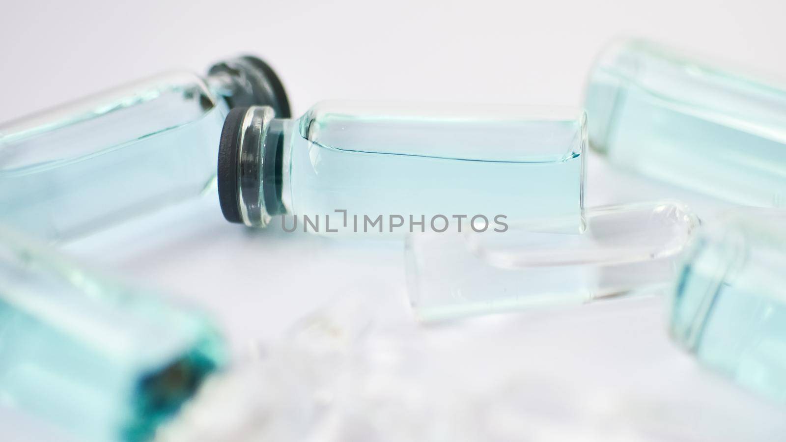 Vial vaccine, top view of glass ampoules with transparent and blue liquid lying on white background, global vaccination concept by balinska_lv
