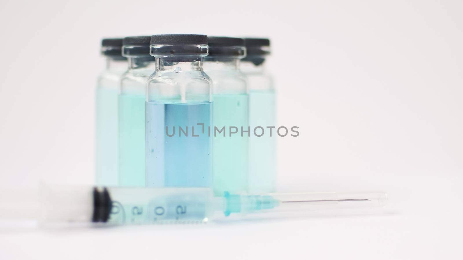 Vial vaccine, glass ampoules with transparent and blue liquid, a syringe is lying near on white background, global vaccination concept.