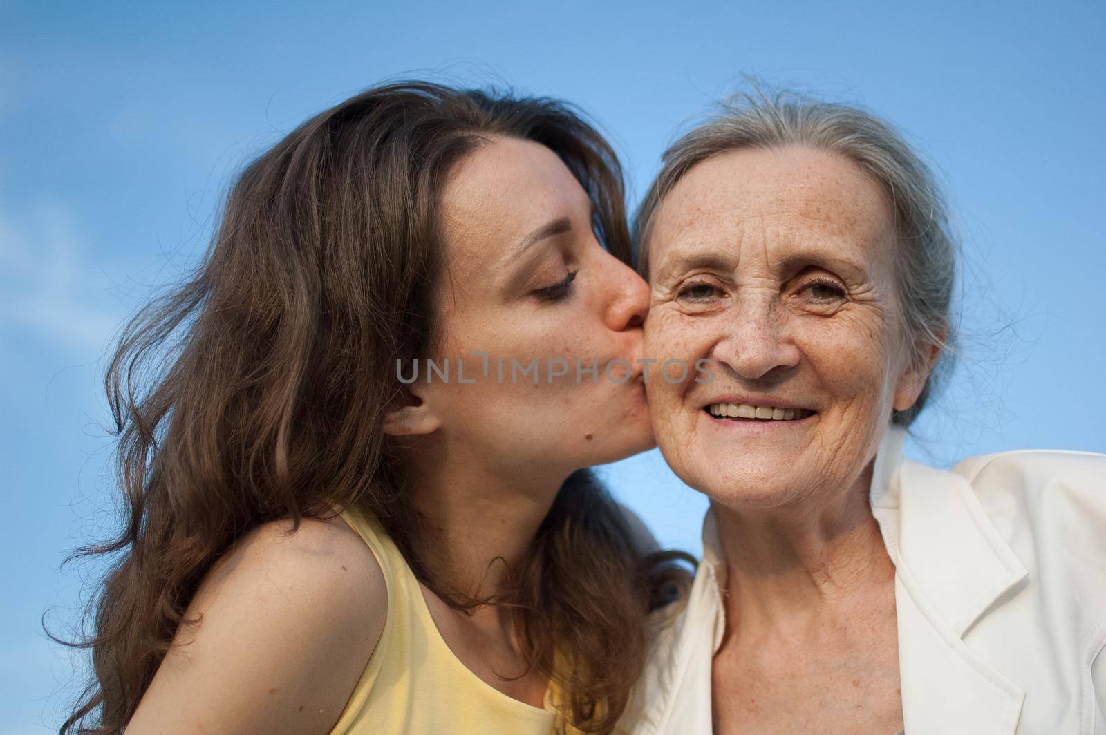 Senior mother with gray hair with her adult daughter looking at the camera in the garden and hugging each other during sunny day outdoors, mothers day by balinska_lv