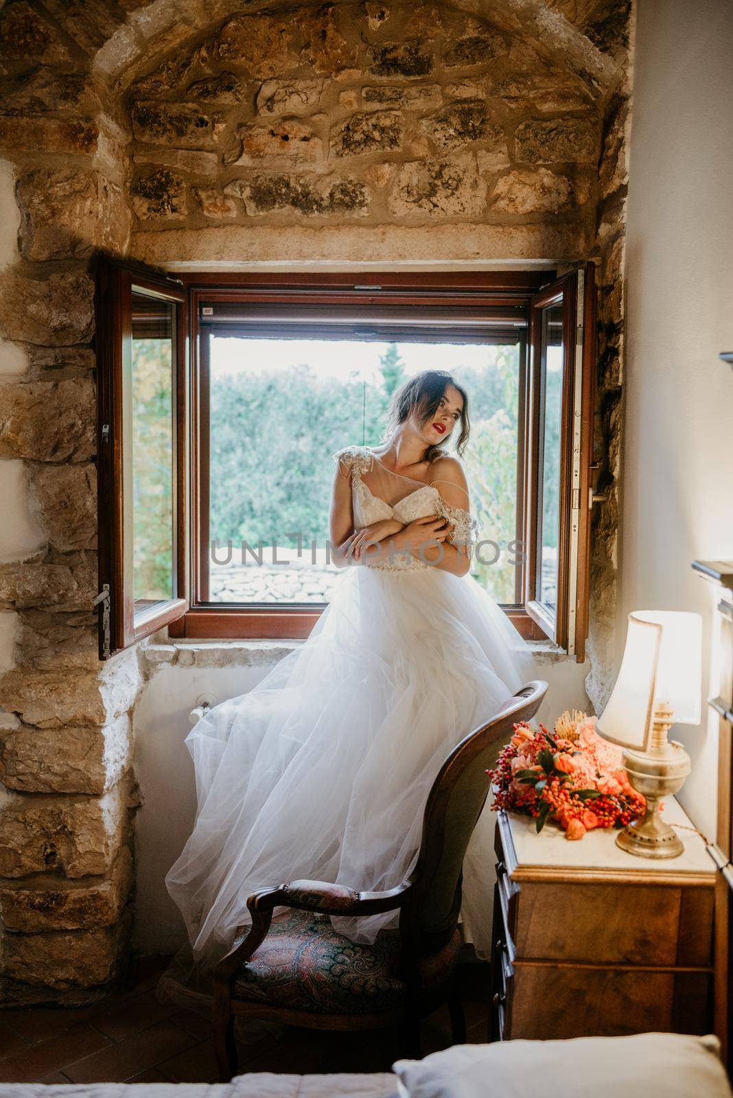 Artistic processing Fantasy girl princess in WHITE WEDDING dress stands in medieval CASTLE room looking vintage window. Bride in a luxury apartment in a wedding dress.. Sweet and gentle girl with fair skin alone in silence in an old castle, spirit of abandoned medieval building whirls in white smoke and magical thick fog in rays of sun