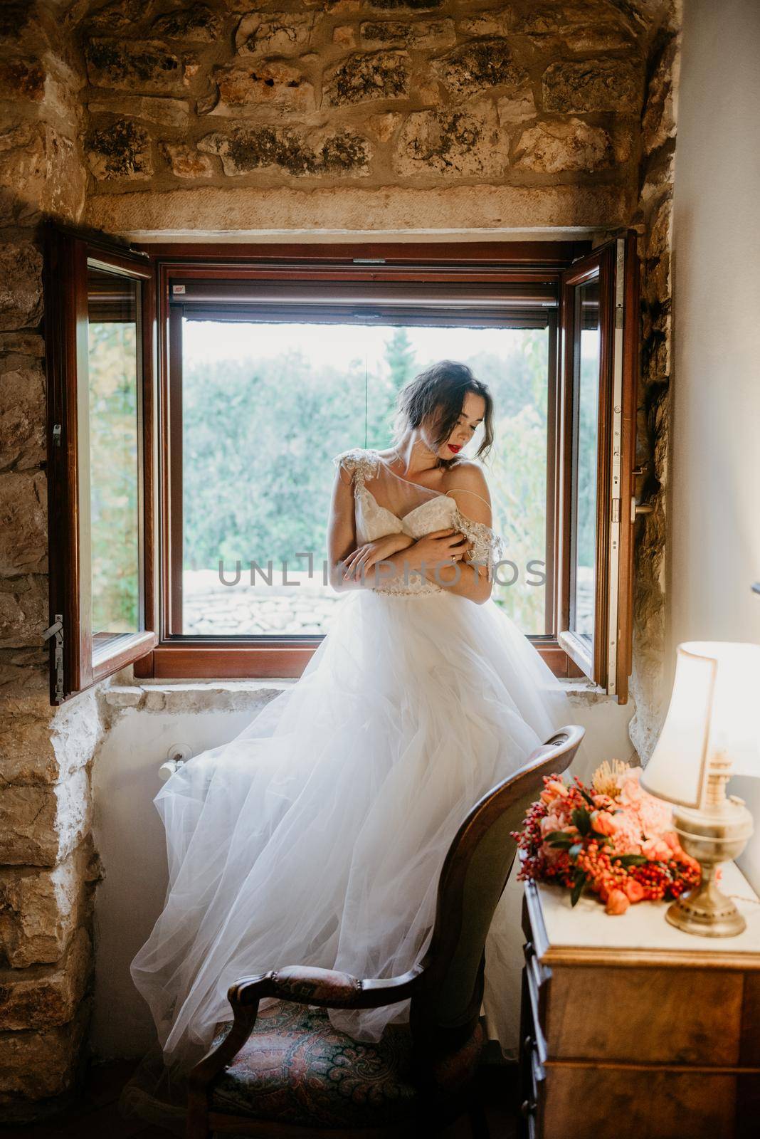 Artistic processing Fantasy girl princess in WHITE WEDDING dress stands in medieval CASTLE room looking vintage window. Bride in a luxury apartment in a wedding dress.. Sweet and gentle girl with fair skin alone in silence in an old castle, spirit of abandoned medieval building whirls in white smoke and magical thick fog in rays of sun