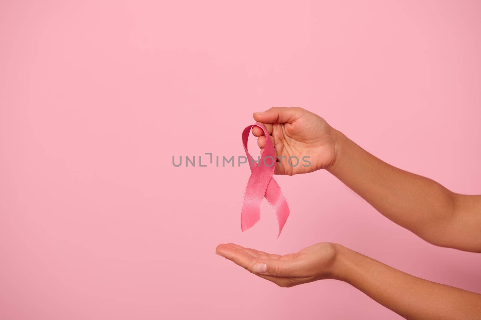 Woman hands holding a pink ribbon, symbol of World Breast Cancer awareness Day, in 1 st October. Woman's health and medical concept, October Pink day, World Cancer Day, national Cancer Survivor Day. by artgf