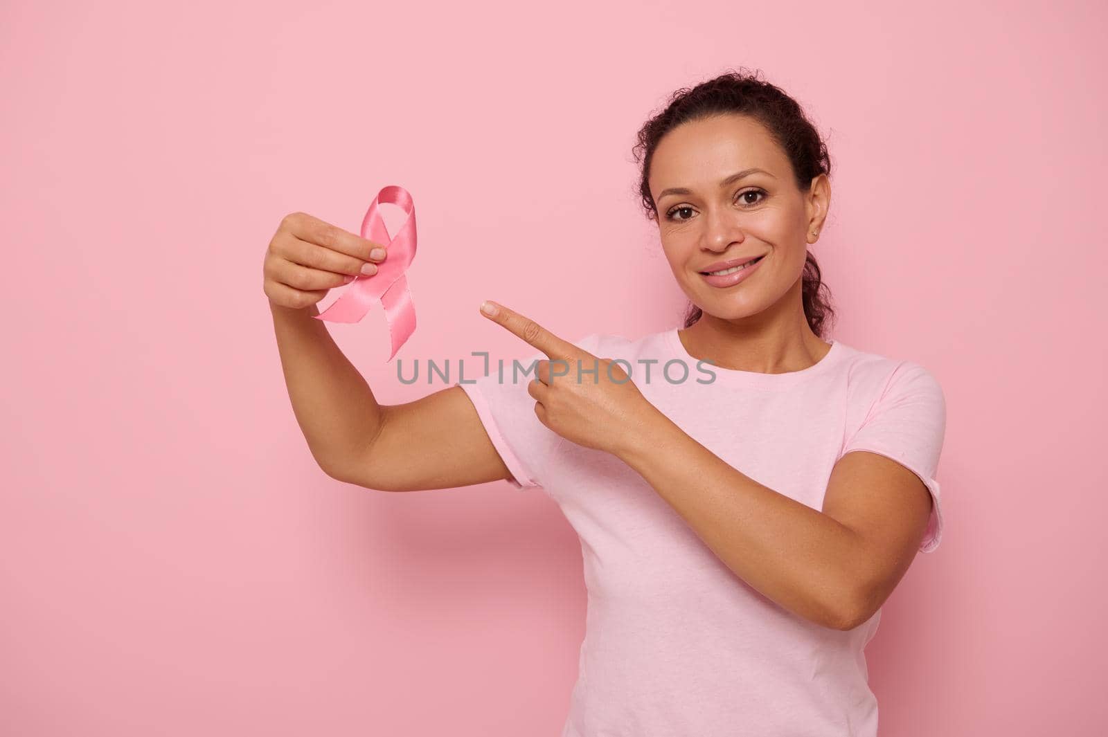Hispanic woman holding a pink ribbon, symbol of World Breast Cancer awareness Day, in 1 st October. Woman's health care concept, October Pink day, World Cancer Day, national Cancer Survivor Day. by artgf