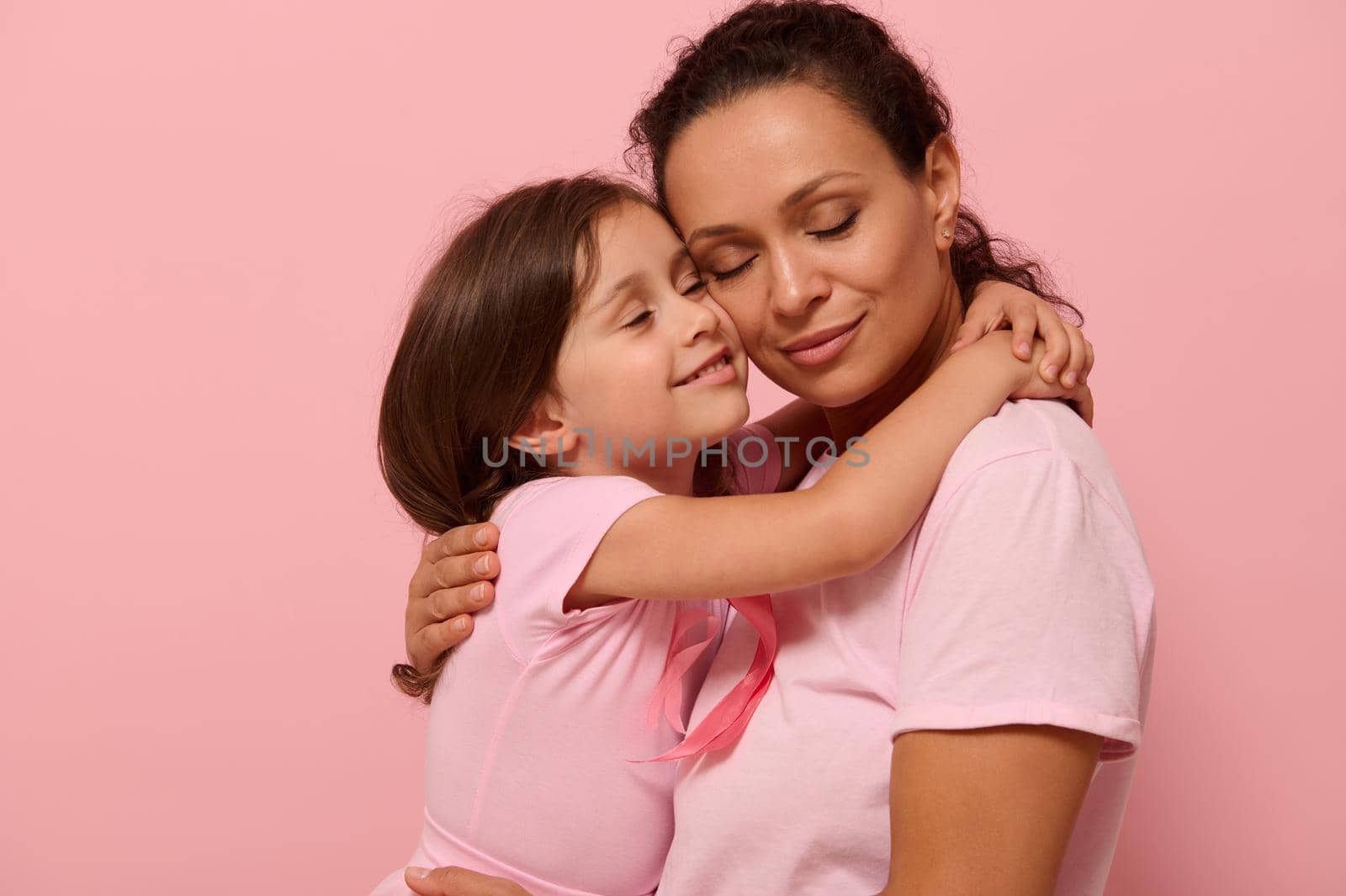 Beautiful loving mother and daughter, hugging each other, wearing pink clothes with a pink ribbon, symbol of World Breast Cancer awareness Day in October. World Cancer Day national Cancer Survivor Day