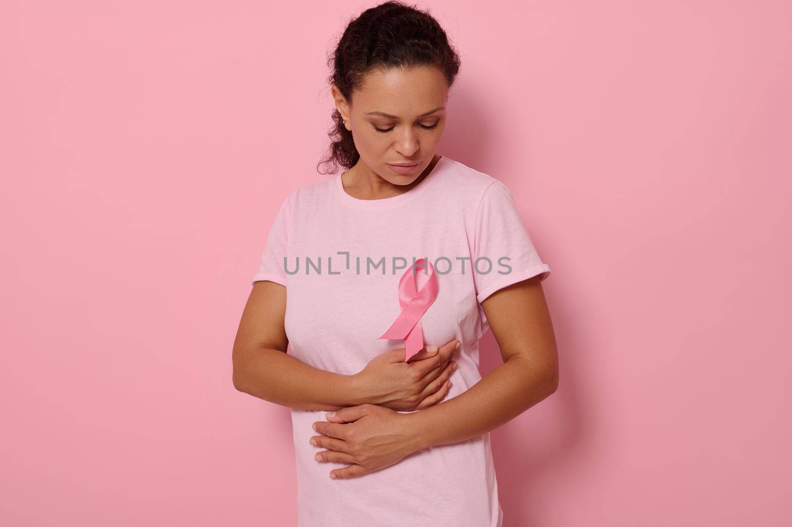 African American woman puts hands under pink ribbon on her pink T Shirt, for breast cancer campaign, supporting Breast Cancer Awareness. Concept of 1 st October Pink Month and women's health care by artgf