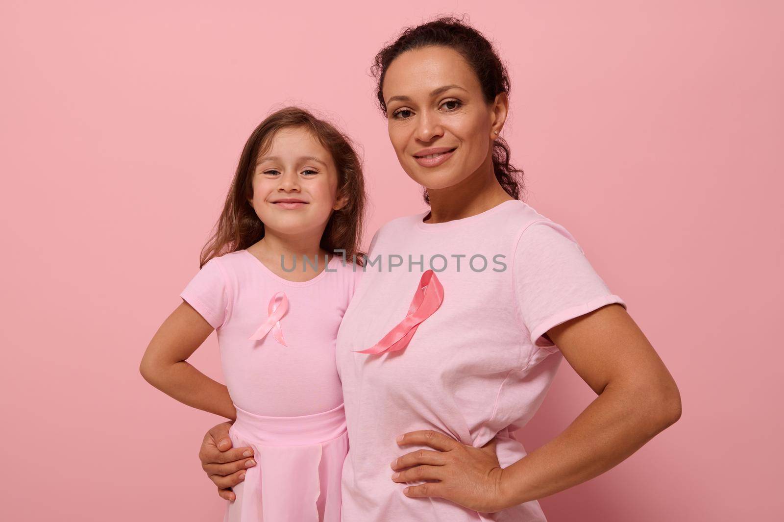 Gorgeous women of two generations, African American lady and European baby girl, in pink clothes and pink ribbon, support cancer survivors. Medical Concept October 1. World Breast Cancer Awareness Day