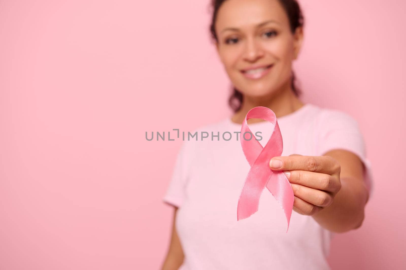 Blurred smiling African woman in pink t-shirt holding satin ribbon in her hand. Breast and abdominal cancer awareness, October Pink day on colored background, copy space. Breast cancer support concept by artgf