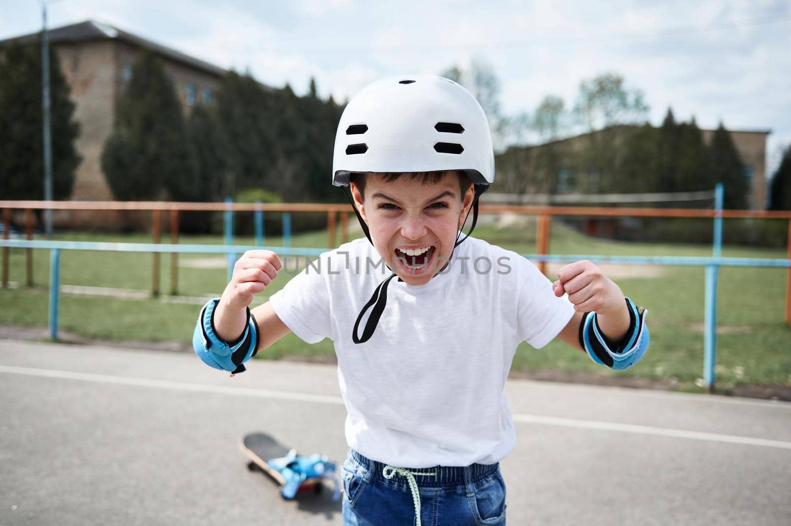 Boy skateboarder in safety helmet screaming and showing fists looking at camera by artgf