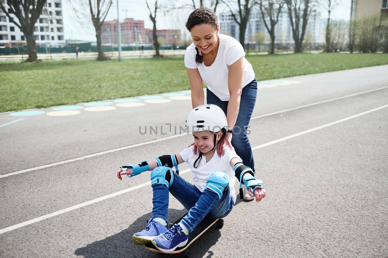 Loving mother behind her son, who sits on a skateboard. Happy childhood and motherhood concept