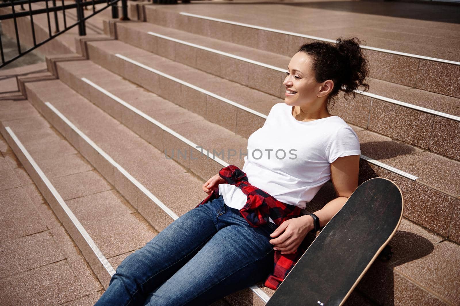Portrait of a young smiling African America woman posing on stairs with skateboard by artgf