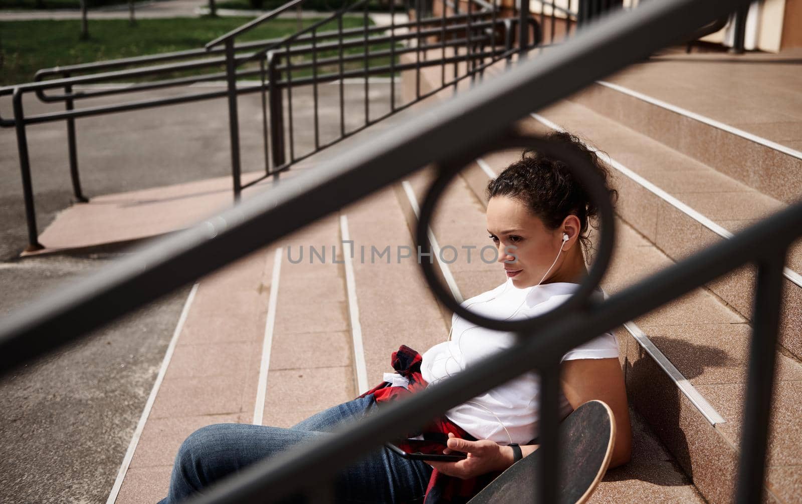 View through the railing of a beautiful Hispanic woman sitting on the steps of an unrecognizable building