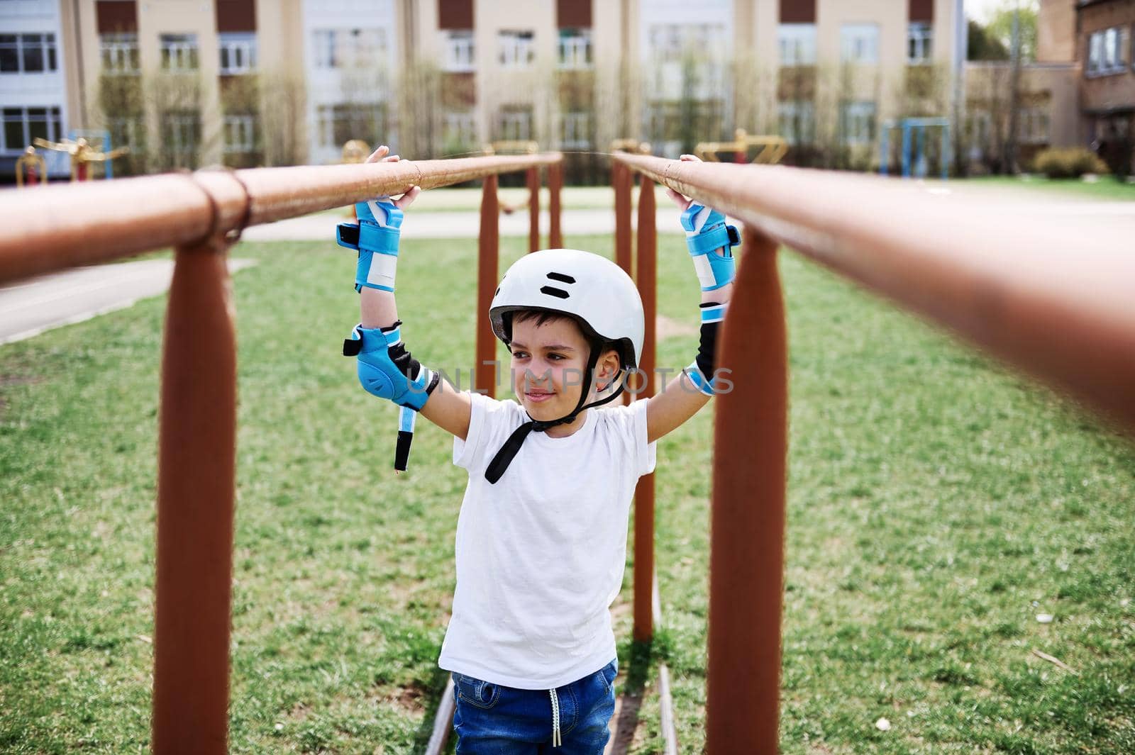 Handsome boy in safety helmet and protective gear between horizontal bars on playground outdoors. Closeup