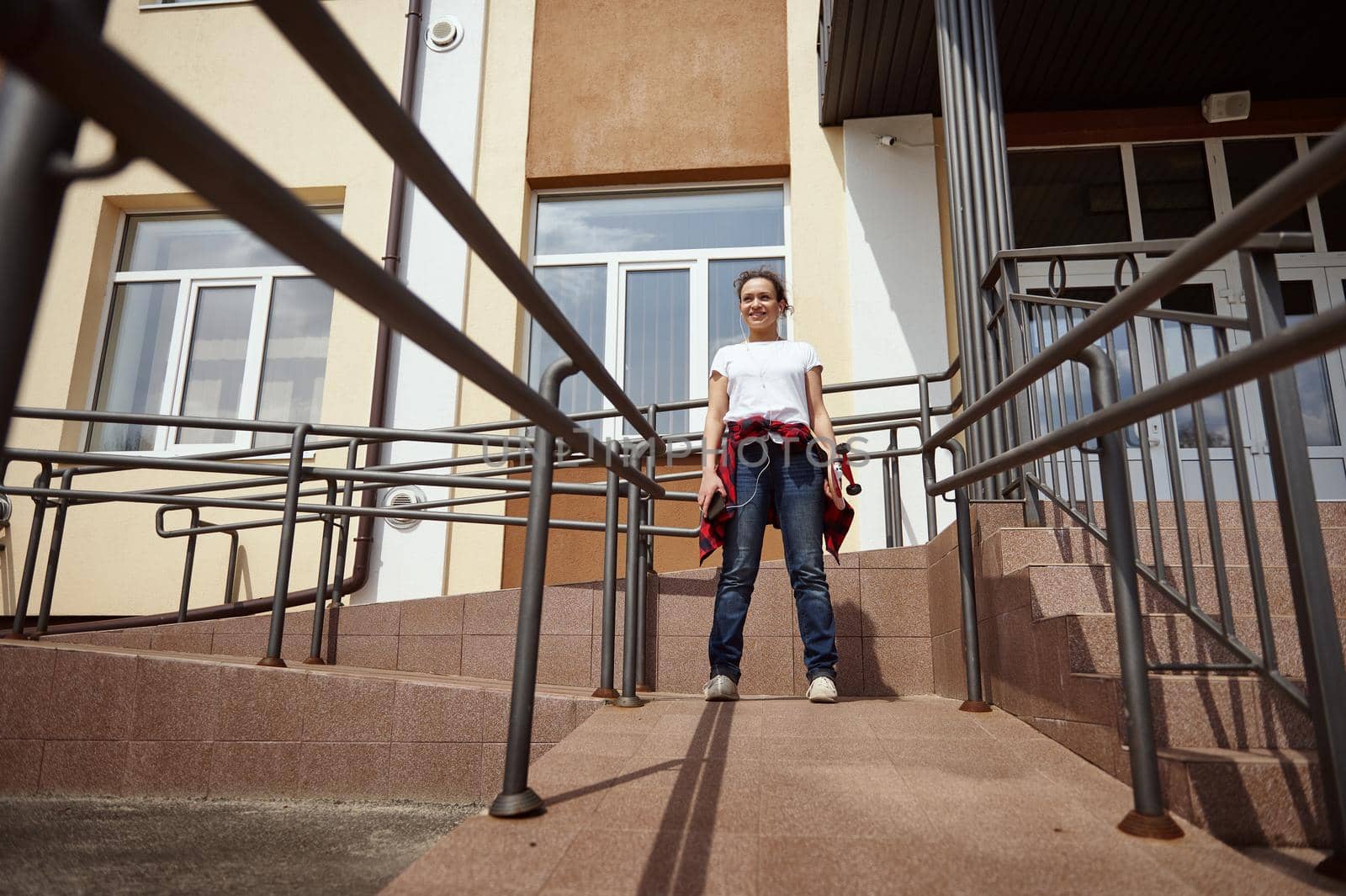 Young mixed race woman with skateboard standing on the background of a yellow building