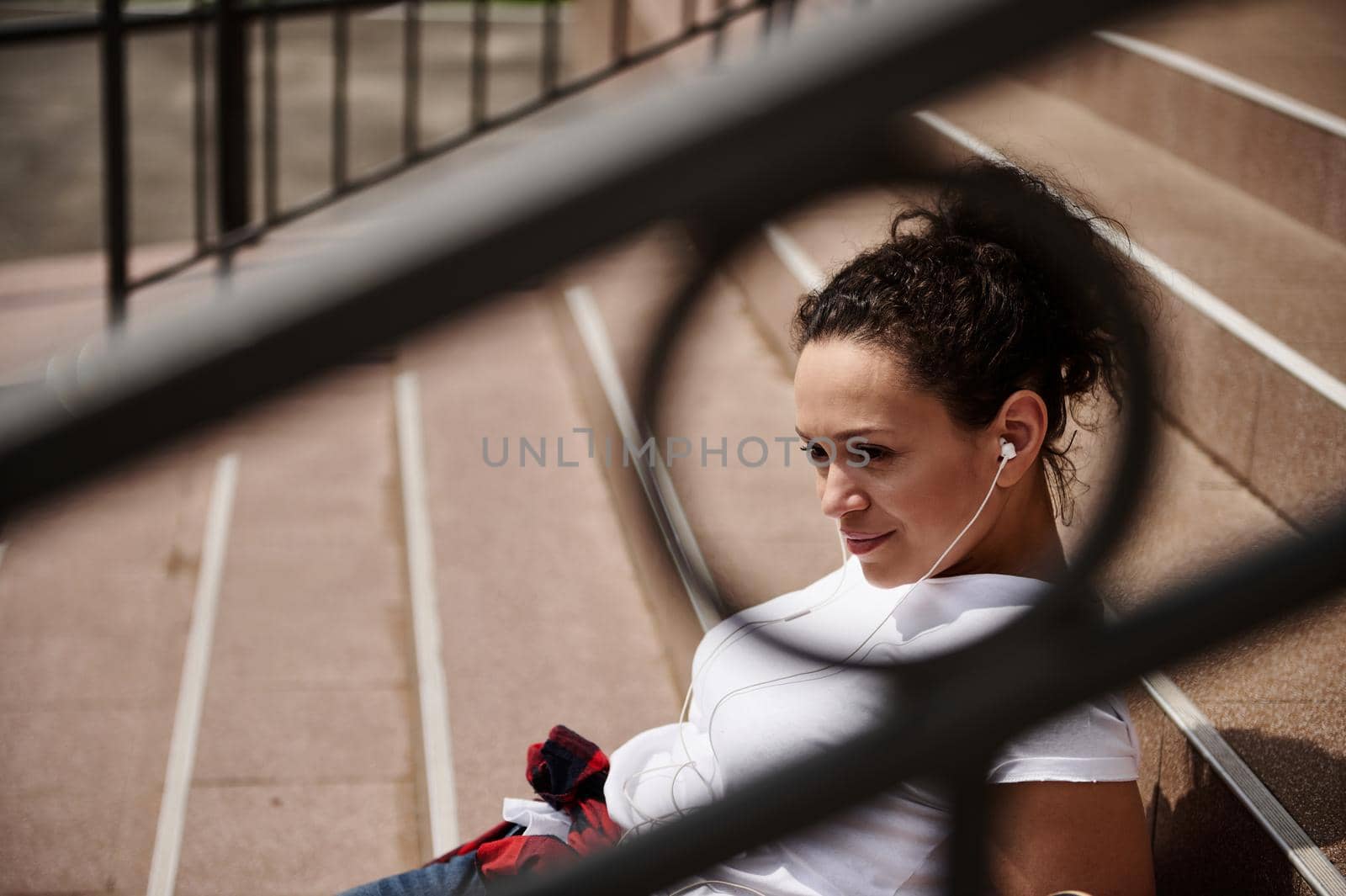 Closeup view through the railing of an attractive Hispanic woman sitting on the steps of an unrecognizable building by artgf