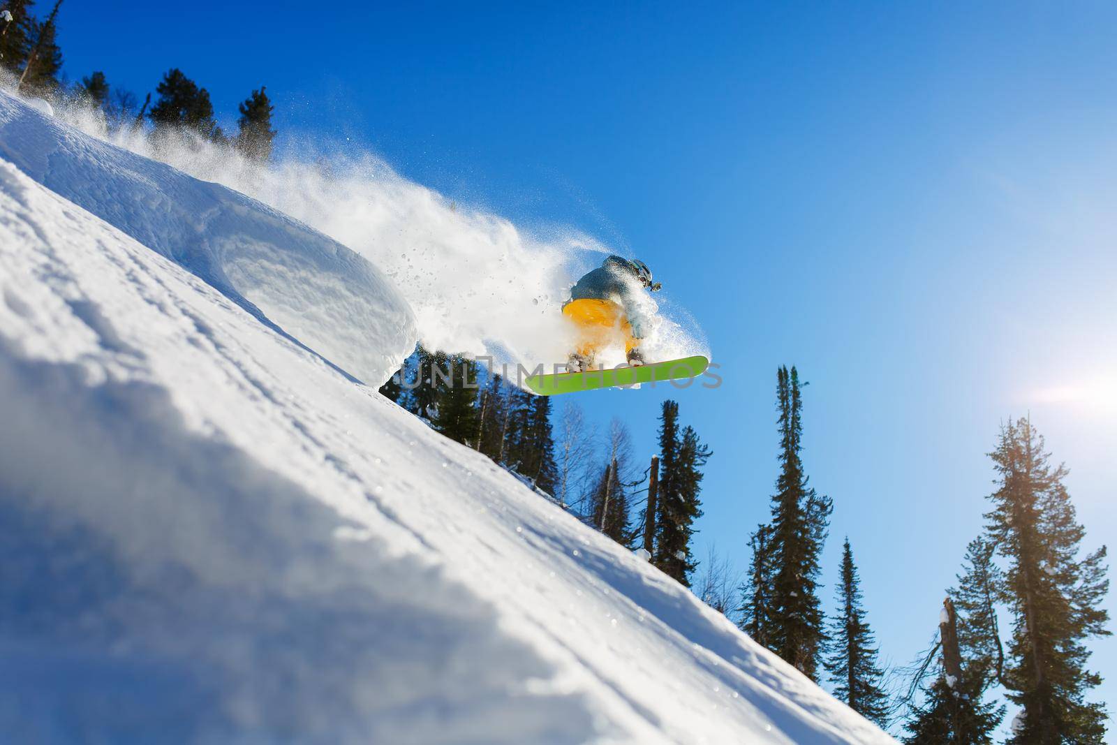 A snowboarder jumps from a springboard in the high mountains on a sunny day. Sun rays, white snow and clear weather, blue sky.