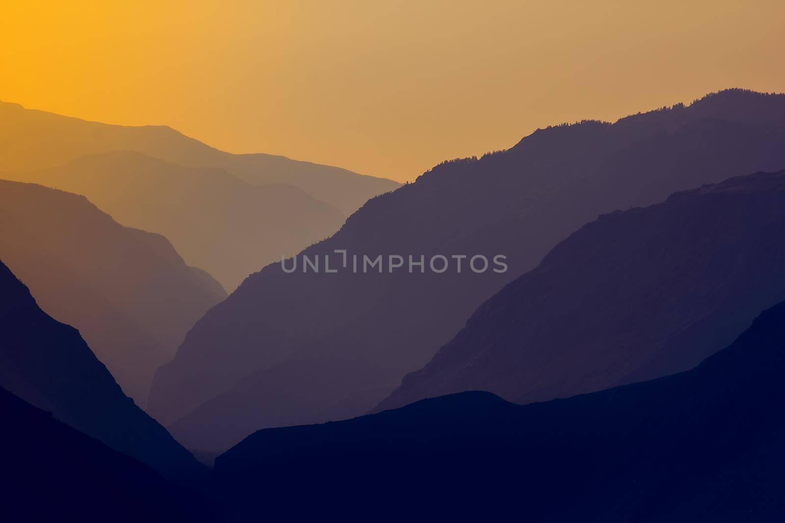 Silhouettes and outlines of a mountain massif in the setting sun. Orange color of the sky. Altai.