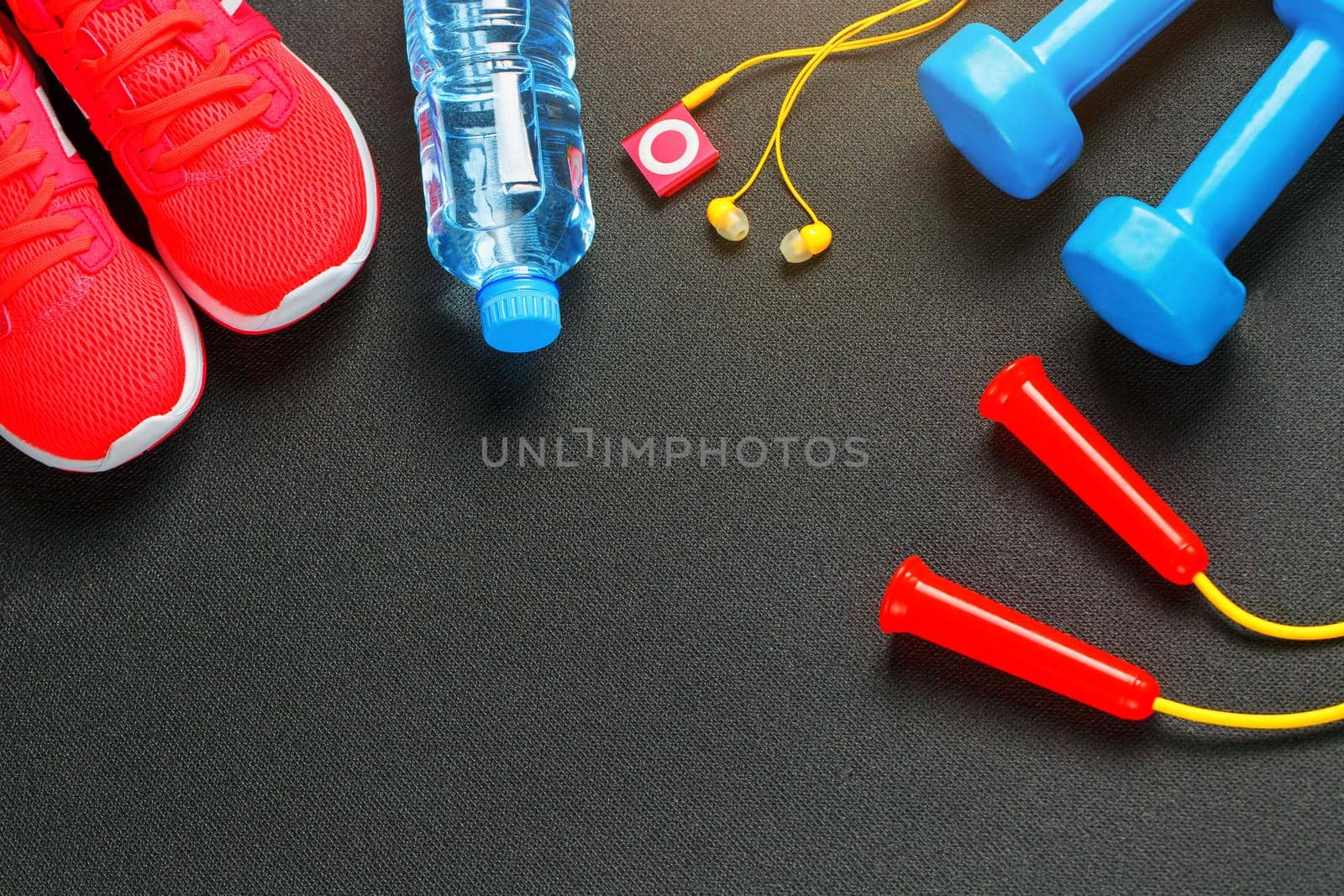 Top view of sports equipment, dumbbells, a skipping rope, a bottle of water, sneakers and a player. Against a gray background