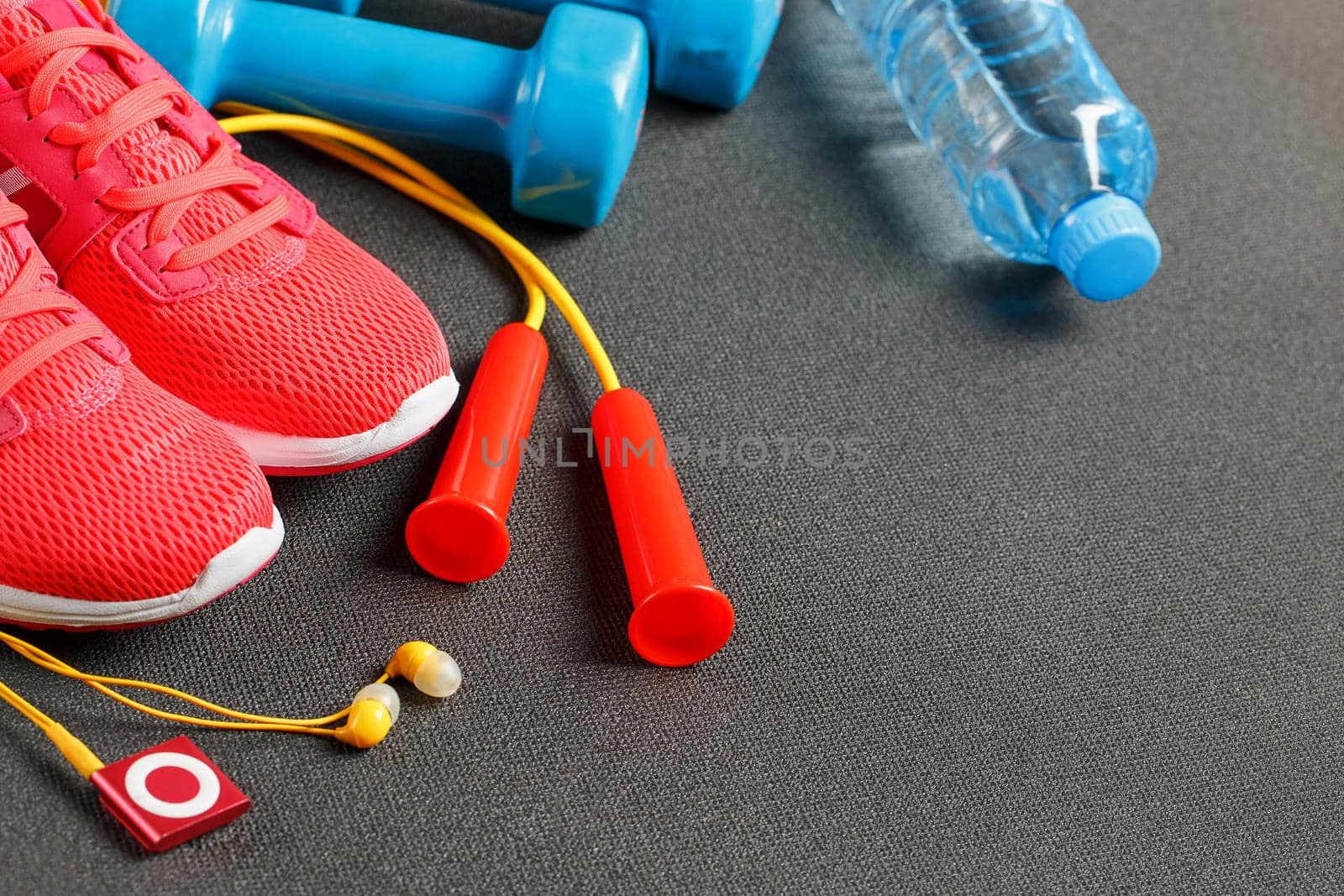 Top view of sports equipment, dumbbells, a skipping rope, a bottle of water, sneakers and a player. Against a gray background