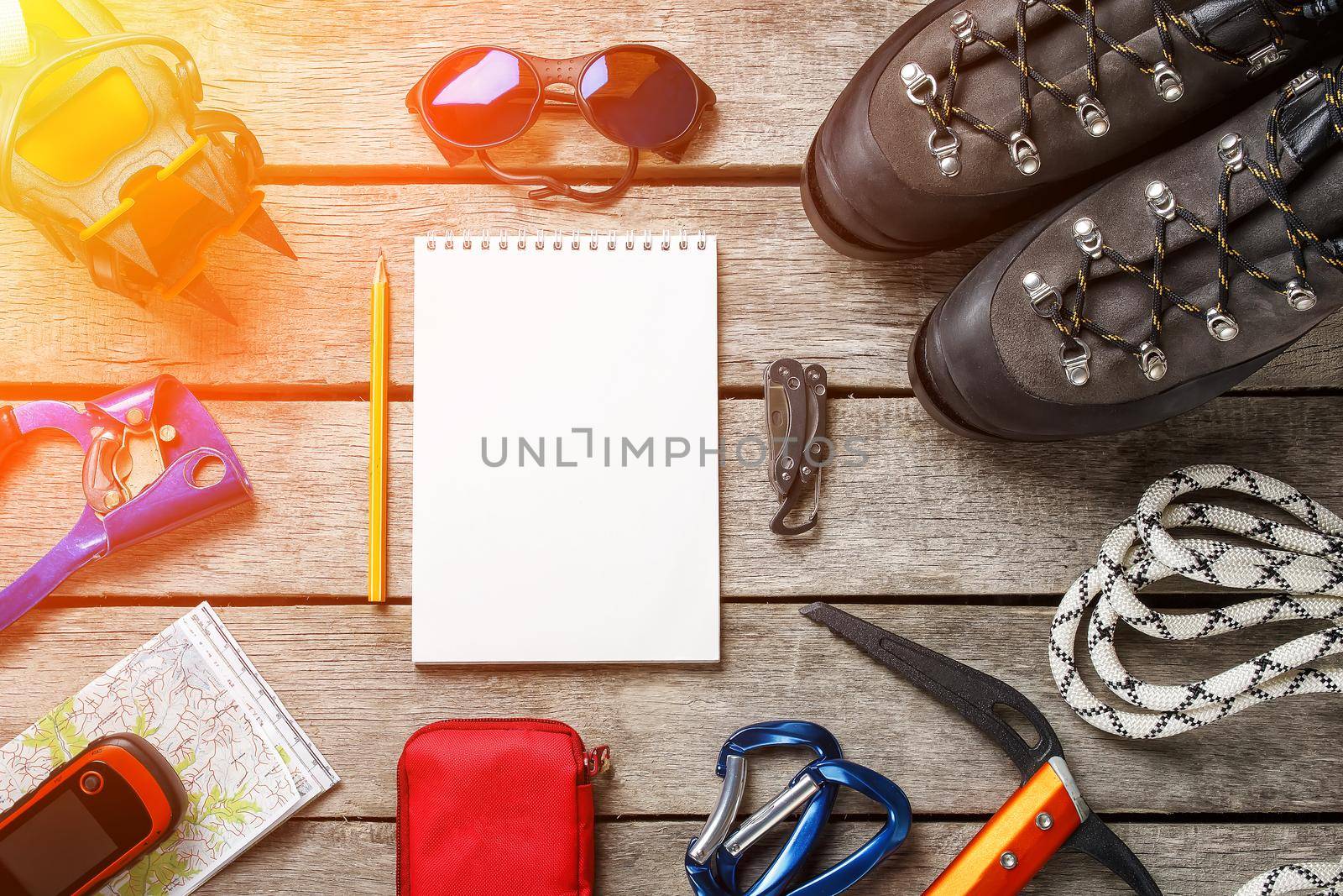 Top view of tourist equipment for a mountain trip on a rustic light wooden floor with a notebook, pencil and empty space in the middle. Top view set. sunlight