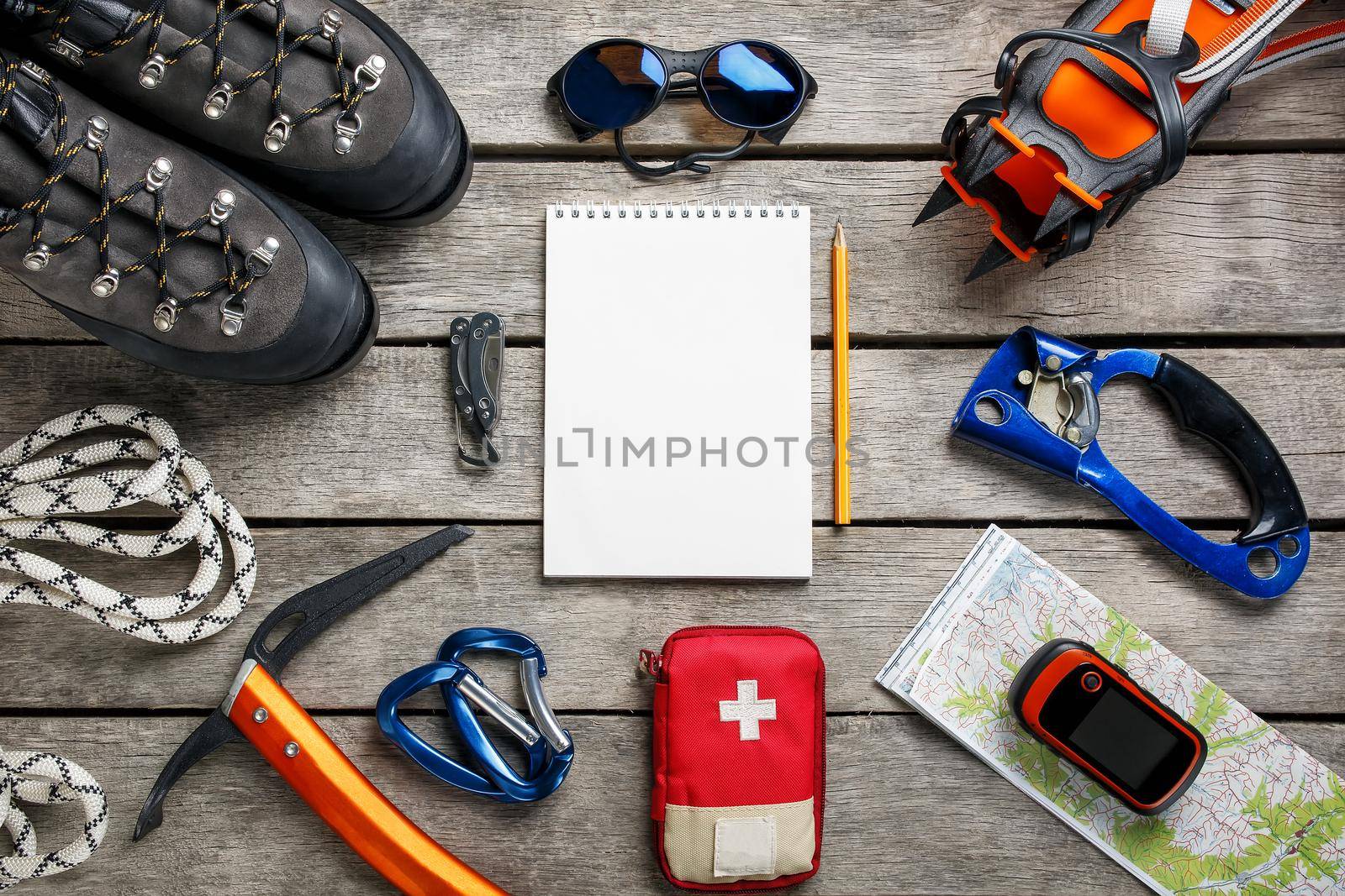 Top view of tourist equipment for a mountain trip on a rustic light wooden floor with a notebook and an empty space in the middle. by AlexGrec