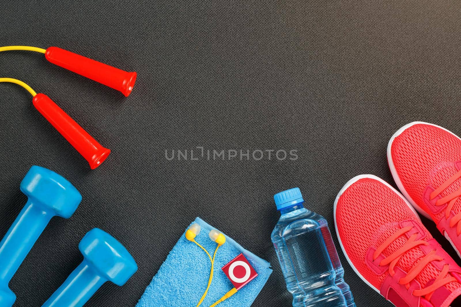 Top view of sports equipment, dumbbells, a skipping rope, a bottle of water, sneakers and a player. Against a gray background