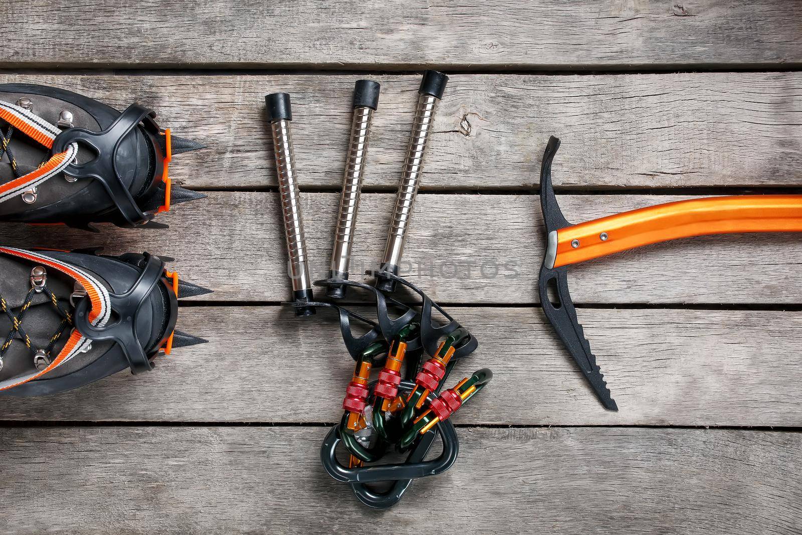 Top view of tourist equipment for a mountain trip on a rustic light wooden floor. Items include glasses, a card, a centipede, a carbine, an ice ax.