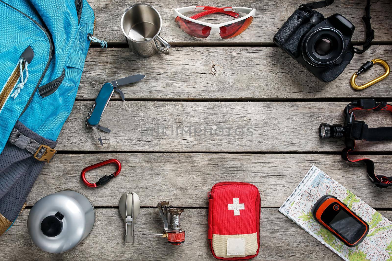 Top view of tourist equipment for travel and tourism on a rustic light wooden floor with an empty space in the middle. by AlexGrec