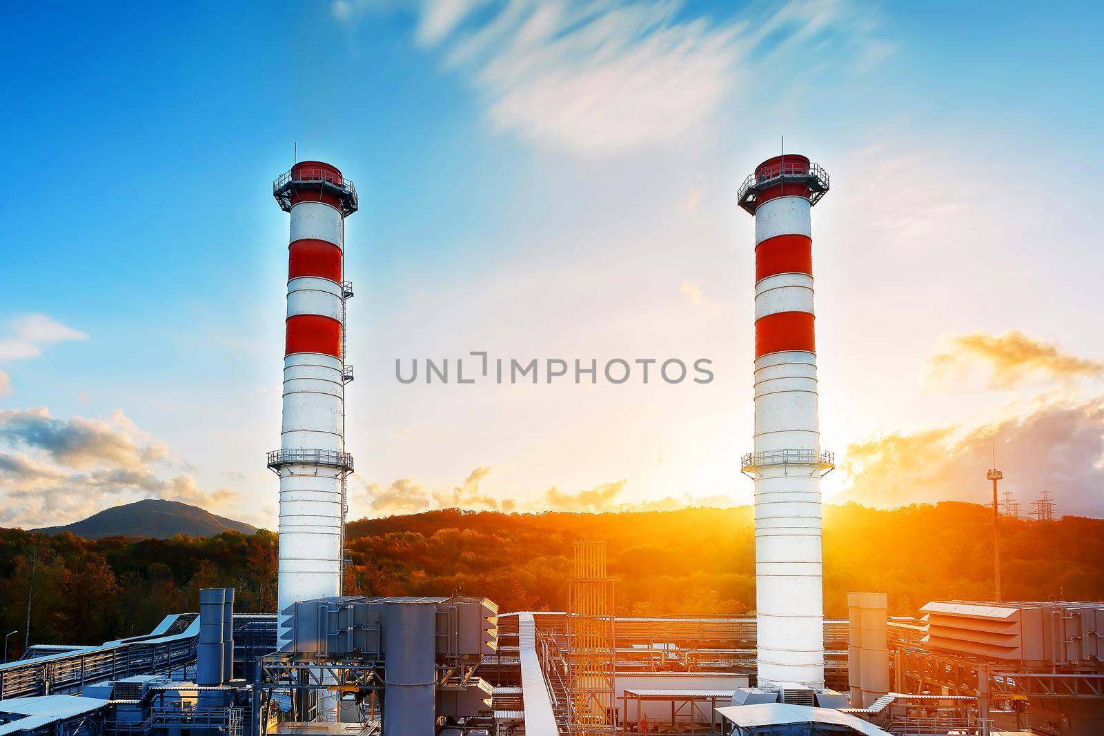 Gas Power Plant with two long pipes of white color with red poloskai on the background of mountains and sunrise in a picturesque environmentally clean place. Power plant area, light industry at sunset. Ecology and low emissions. Clean energy