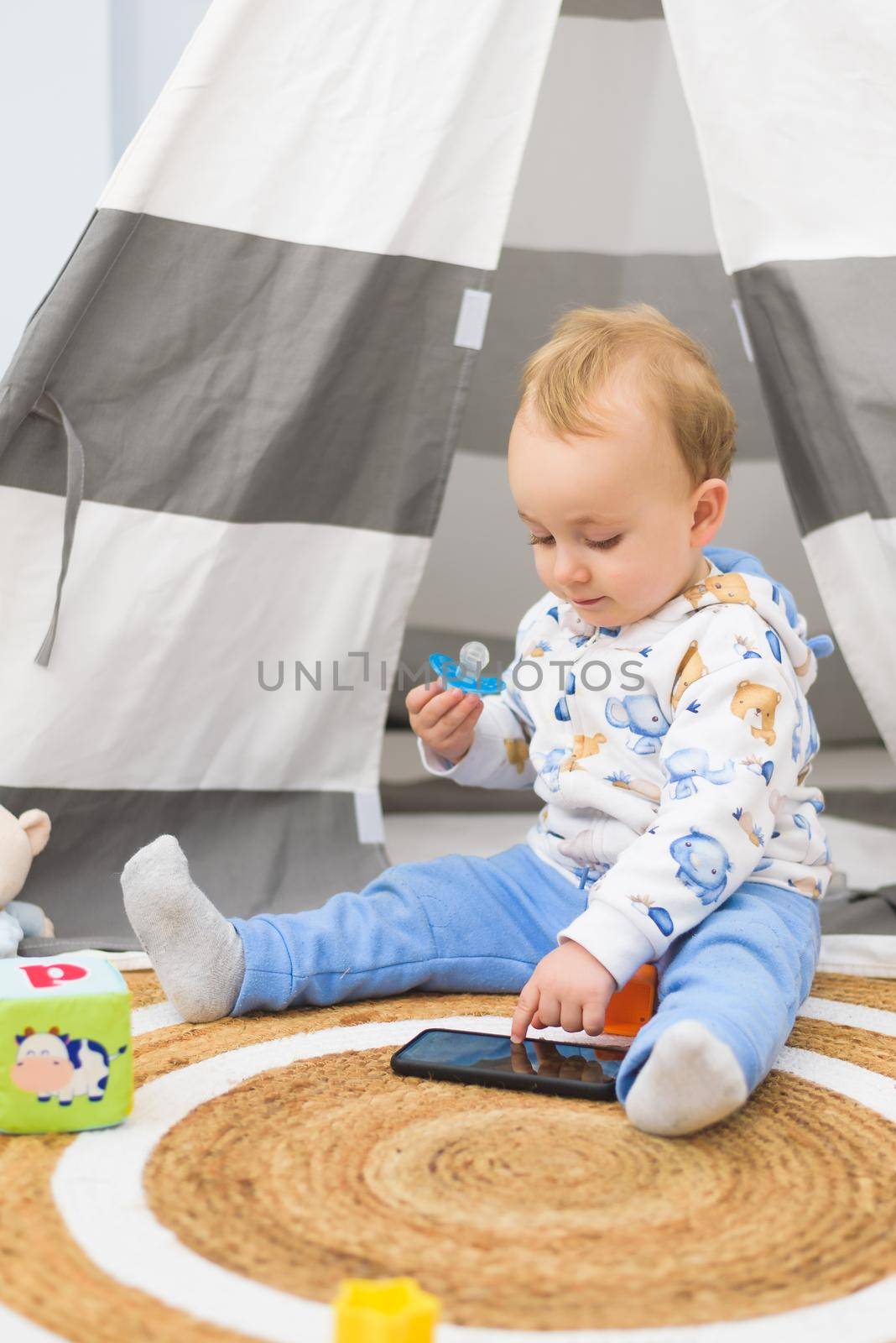 baby playing in his room with his toys and looking at the mobile phone by jcdiazhidalgo