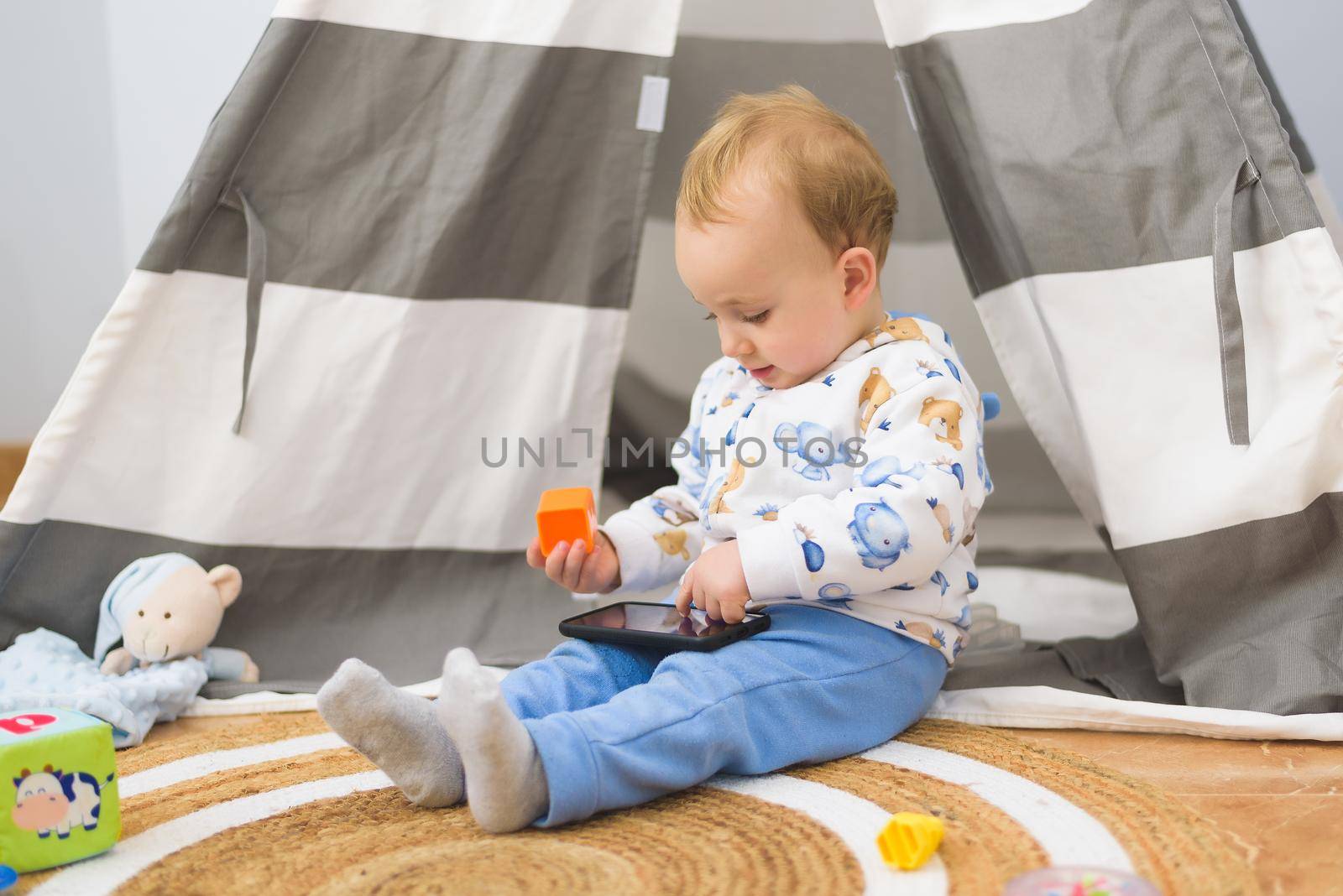 baby playing in his room with his toys and looking at the mobile phone.