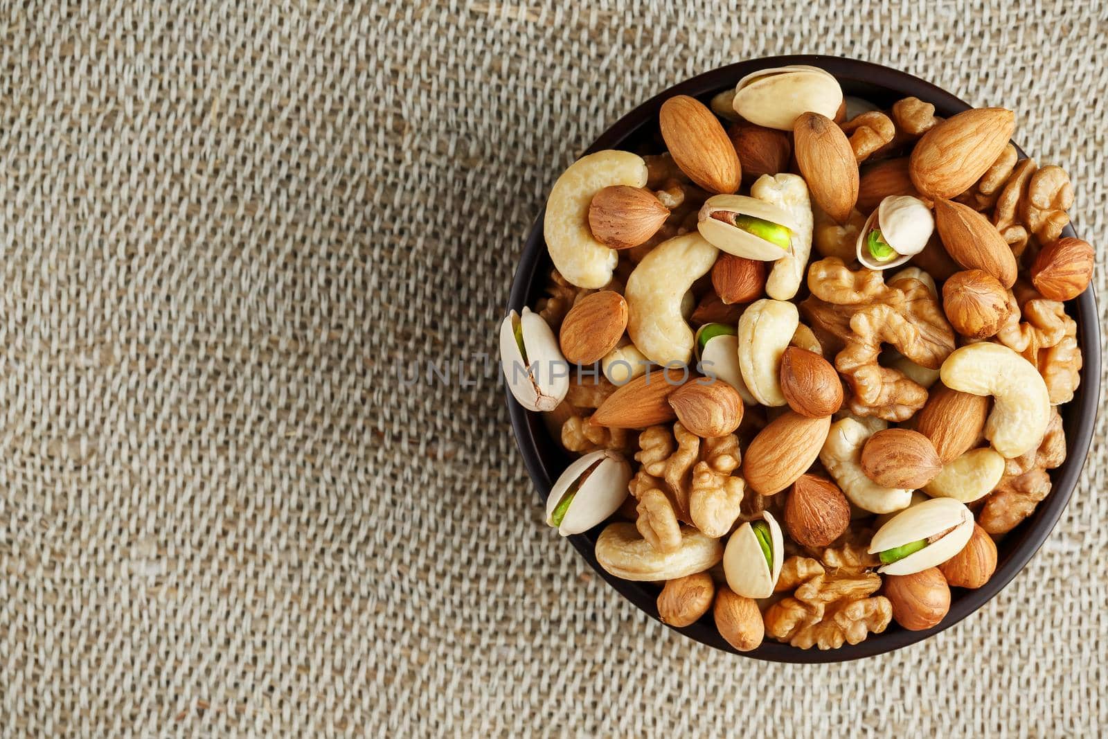 Mix of nuts of cashew, almonds, pistachios, hazelnuts and walnuts is against the background of brown fabric of burlap. Nuts as structure and background, macro