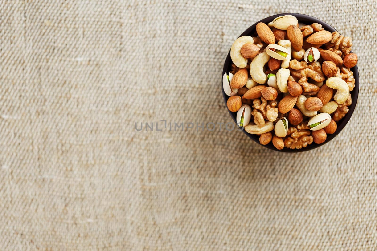 Mix of nuts of cashew, almonds, pistachios, hazelnuts and walnuts is against the background of brown fabric of burlap. Nuts as structure and background, macro