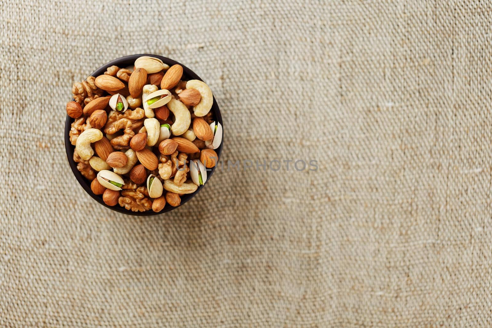 Mix of nuts of cashew, almonds, pistachios, hazelnuts and walnuts is against the background of brown fabric of burlap. Nuts as structure and background, macro