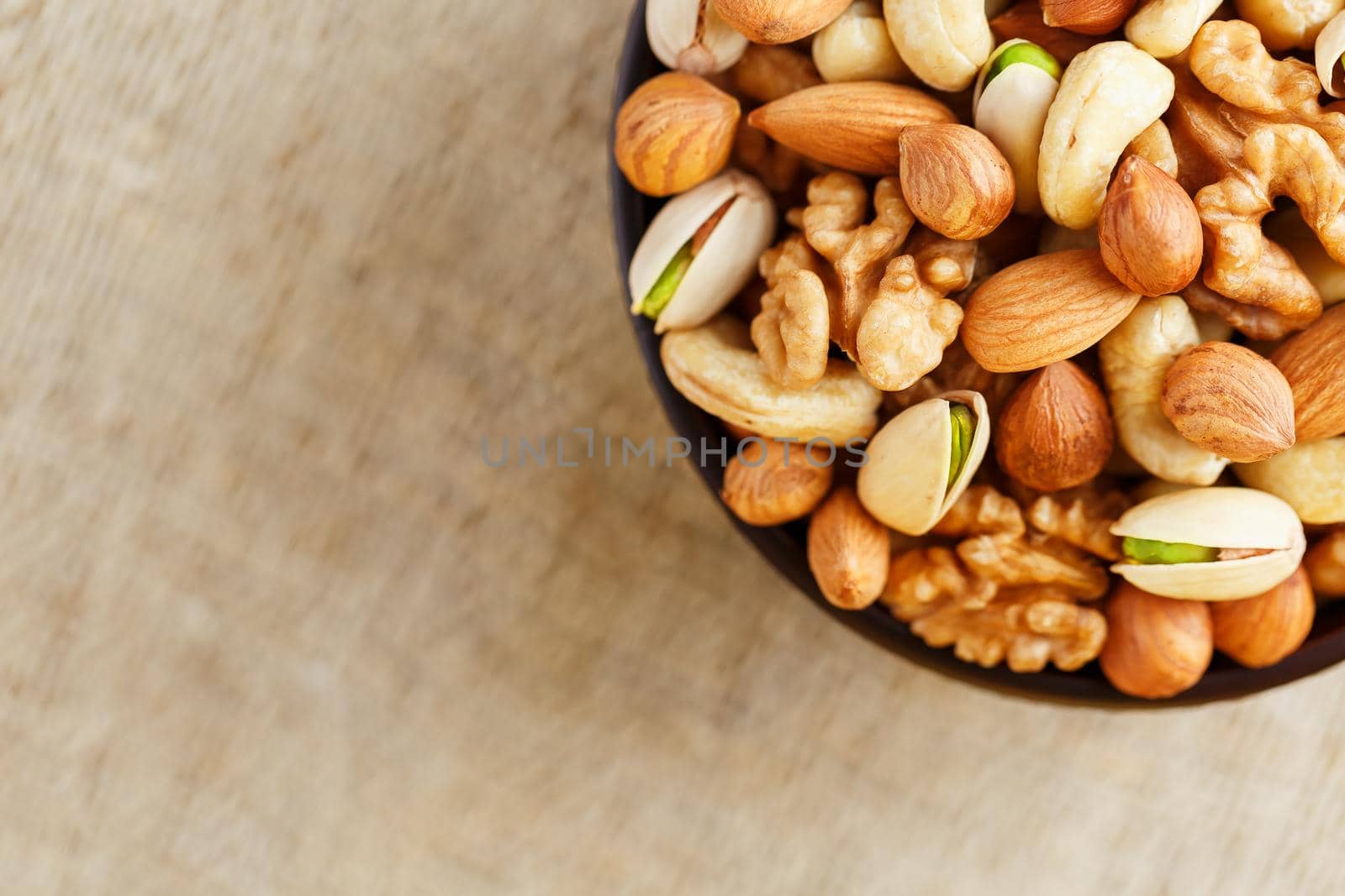 Mix of nuts of cashew, almonds, pistachios, hazelnuts and walnuts is against the background of brown fabric of burlap. Nuts as structure and background, macro