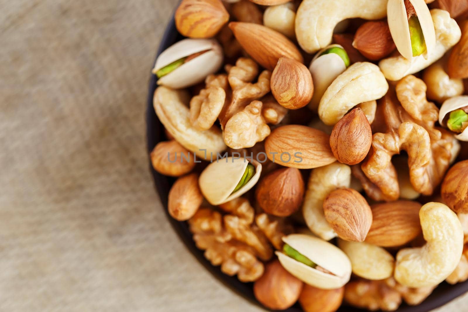 Mix of nuts of cashew, almonds, pistachios, hazelnuts and walnuts is against the background of brown fabric of burlap. Nuts as structure and background, macro